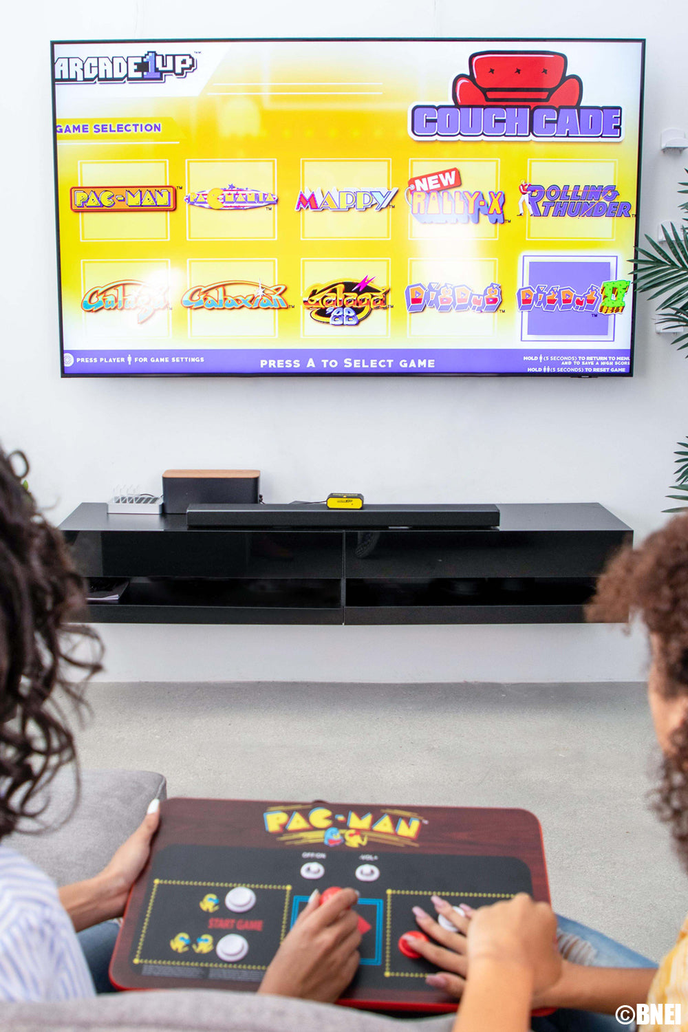 Due persone che giocano a Pac-Man arcade su una TV con un mobile Couchcade.