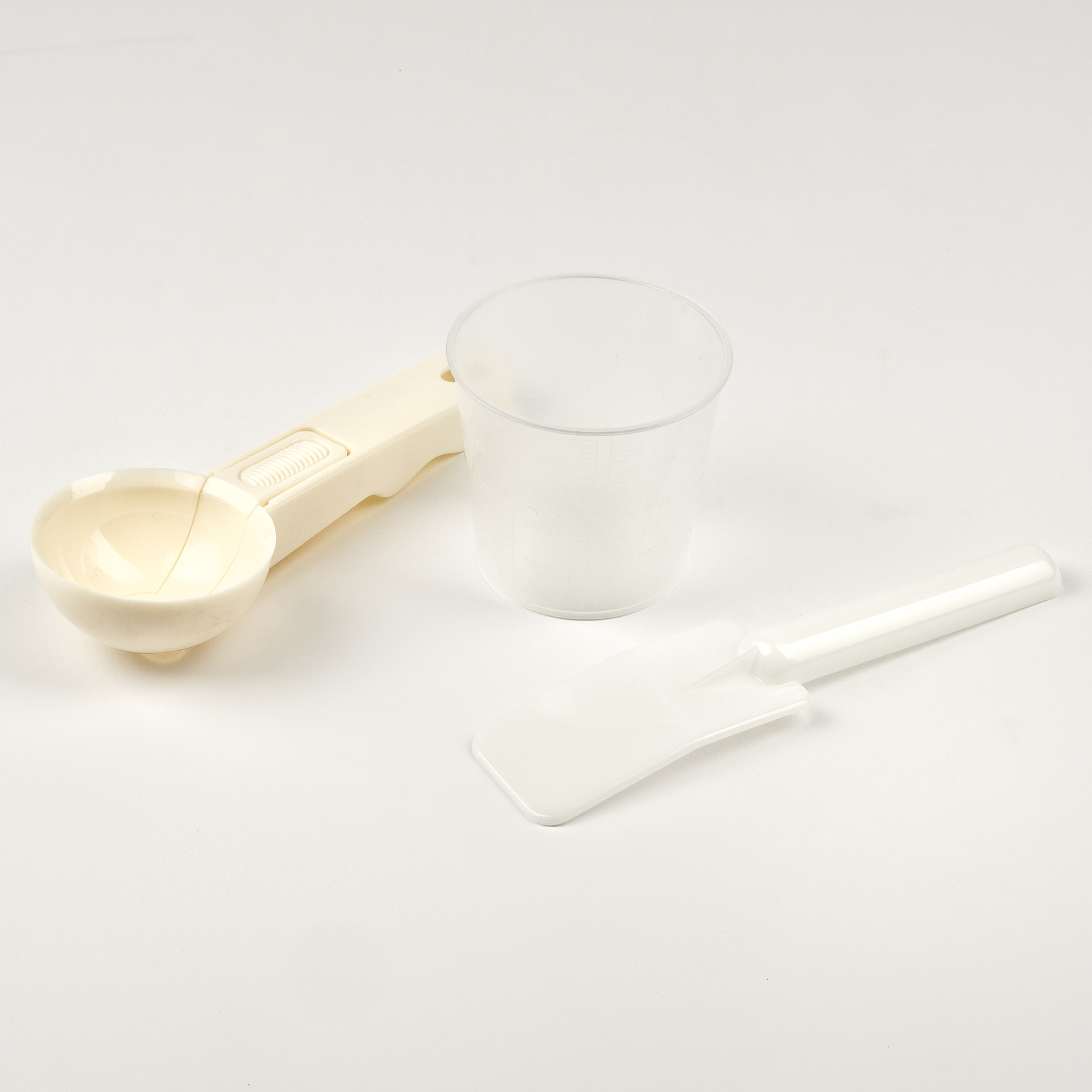 Eisportionierer und Spatel, beide beige, neben einem durchsichtigen Plastikbecher. Alles auf weißem Untergrund.