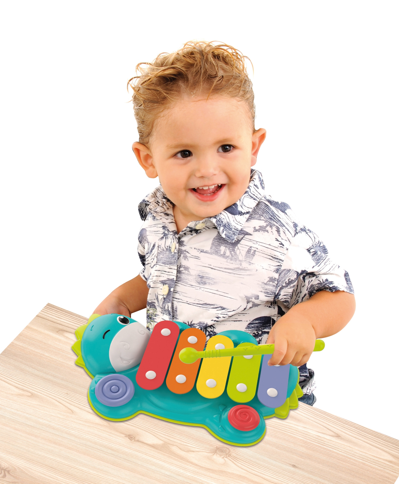 Uśmiechnięte małe dziecko bawi się zabawką-ksylofonem. Leży na drewnianej fakturze, białe tło.