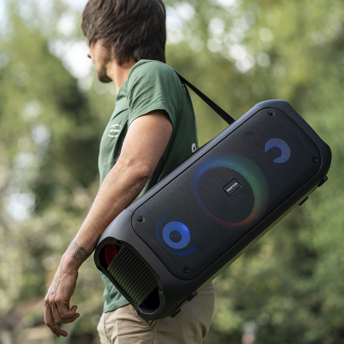 Mężczyzna niosący czarny głośnik z kolorowymi światłami na ramieniu. Zielone tło.