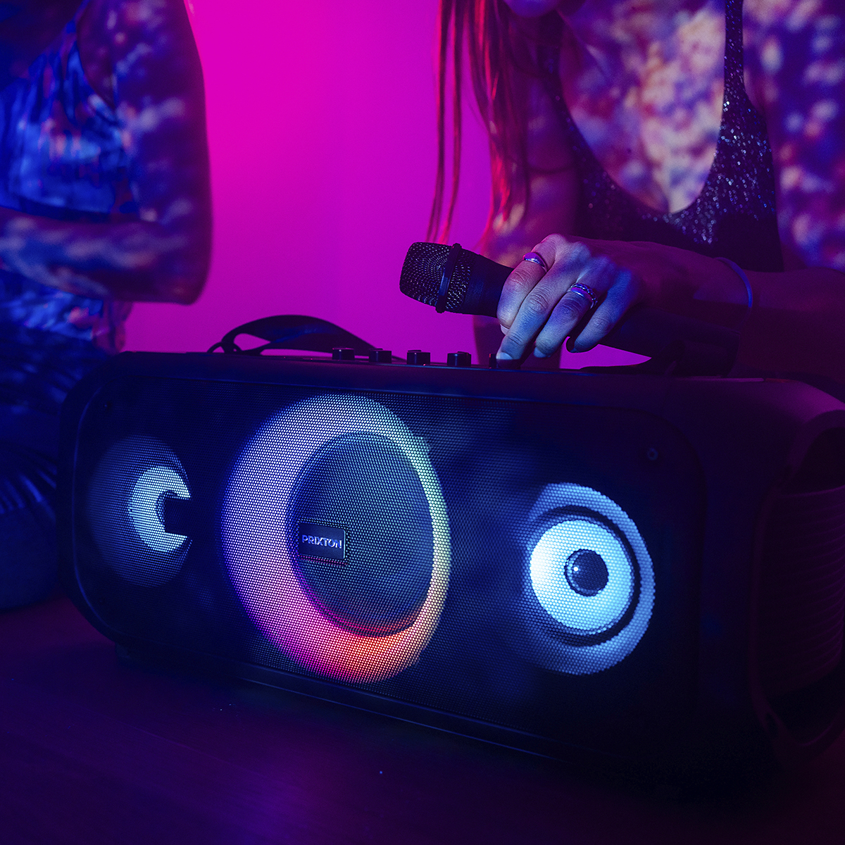 Osoba śpiewa do mikrofonu przed głośnikiem z kolorowymi światłami.