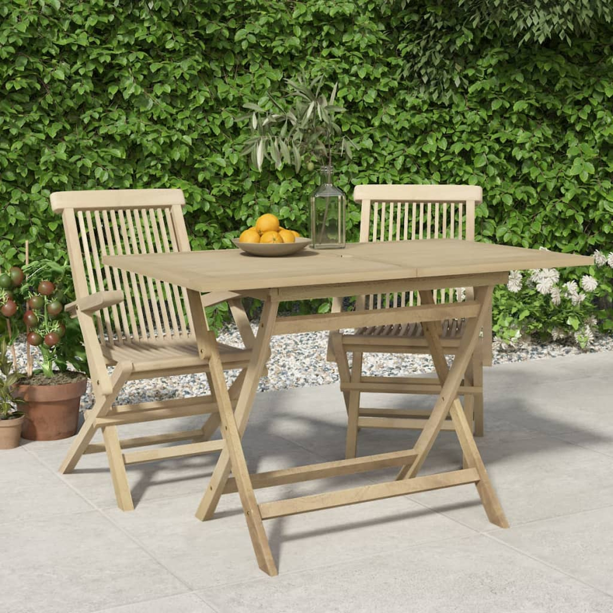 Holztisch und zwei Stühle auf einer Terrasse, mit Laub im Hintergrund.