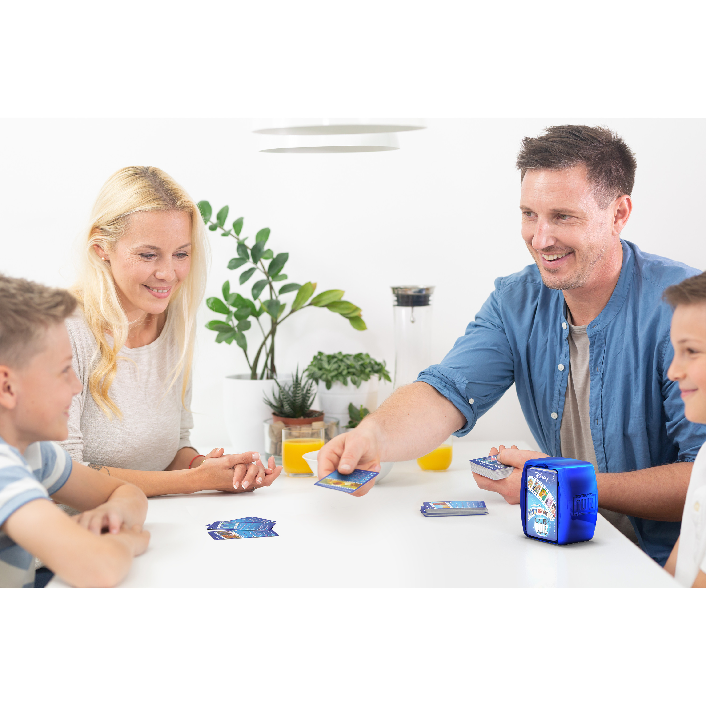 Famille jouant à un jeu de cartes. Une boîte de quiz bleue sur la table. Des cartes sont distribuées.