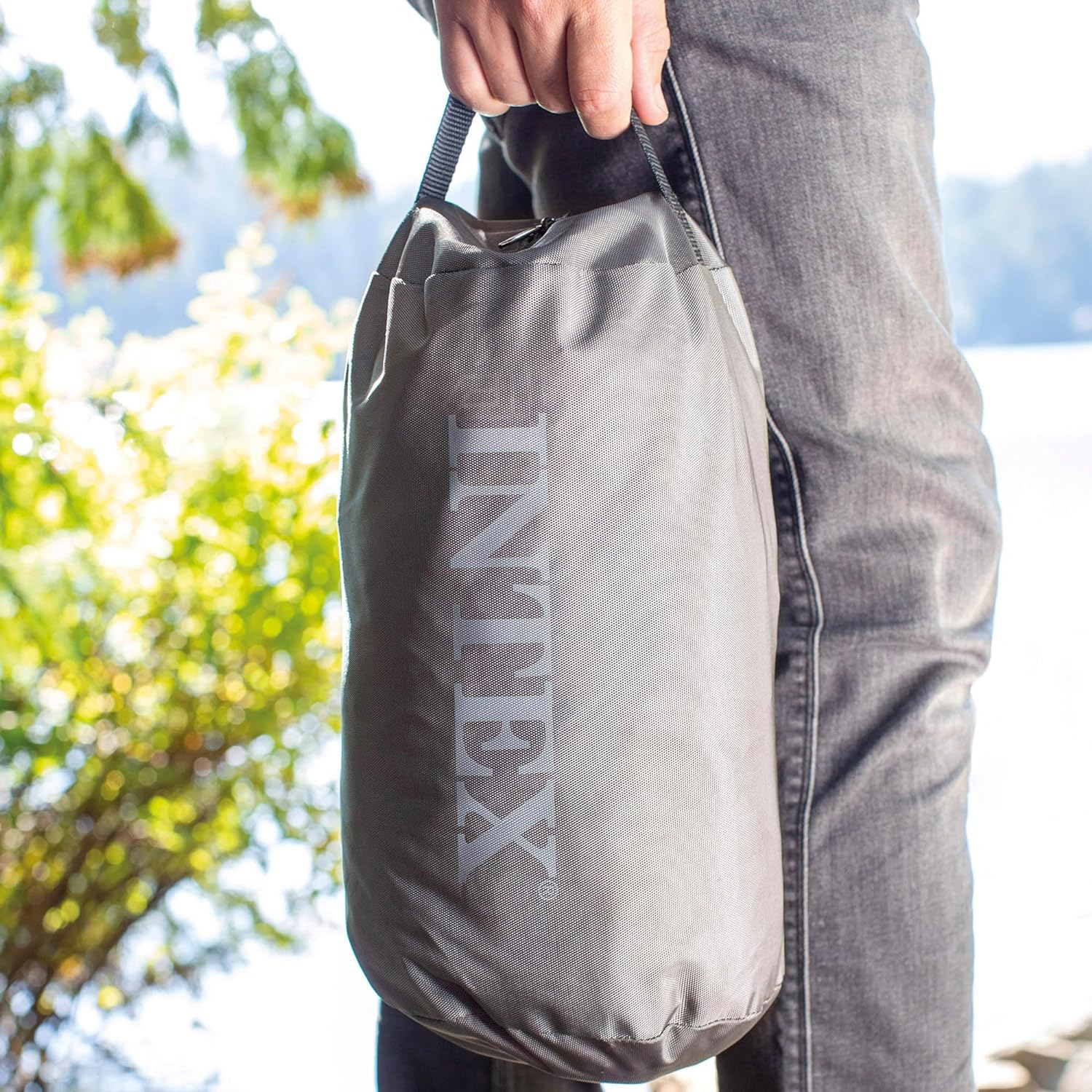 Person hält graue Intex-Tasche mit Bäumen im Hintergrund.