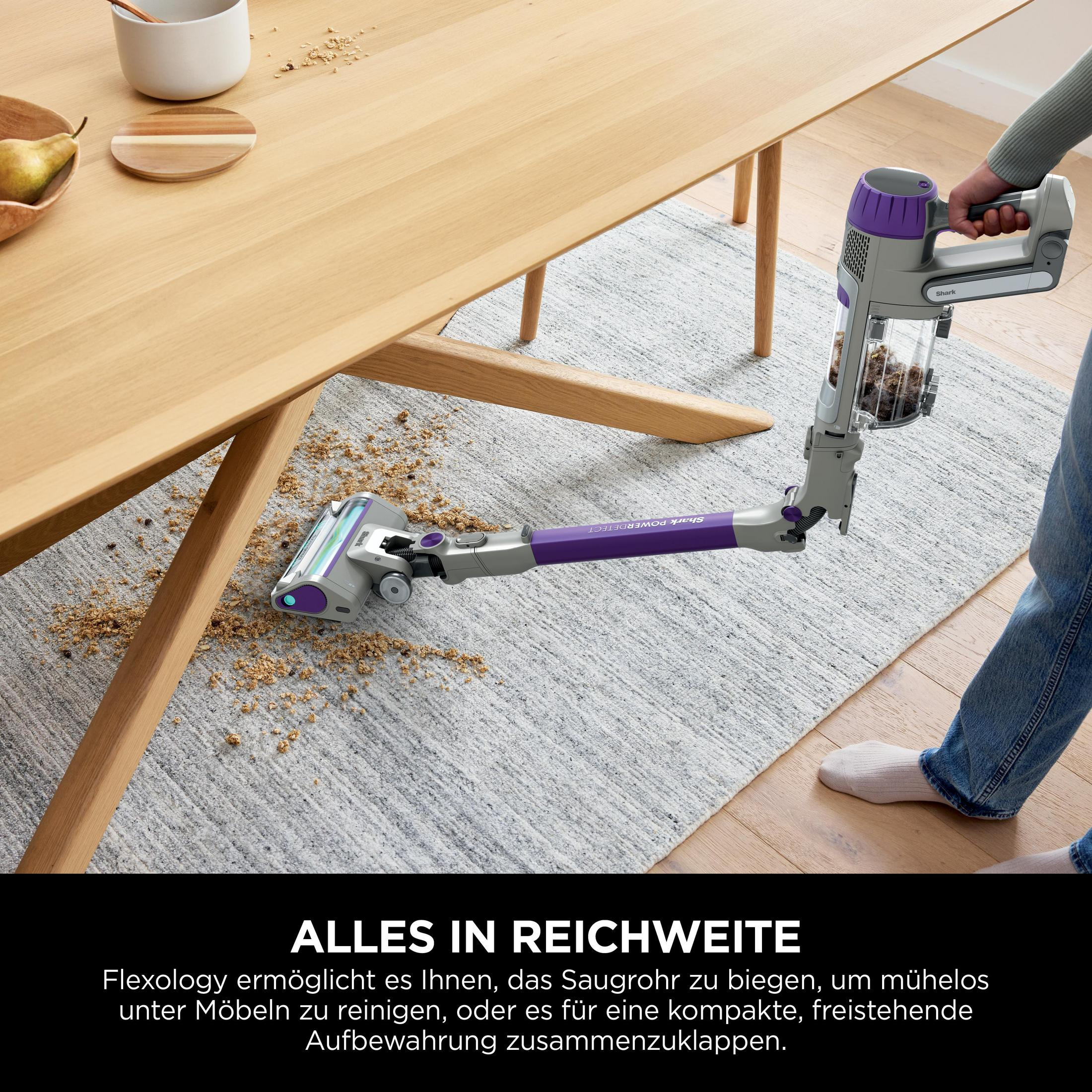 A person using a purple and gray vacuum cleaner on a rug near a wooden table.