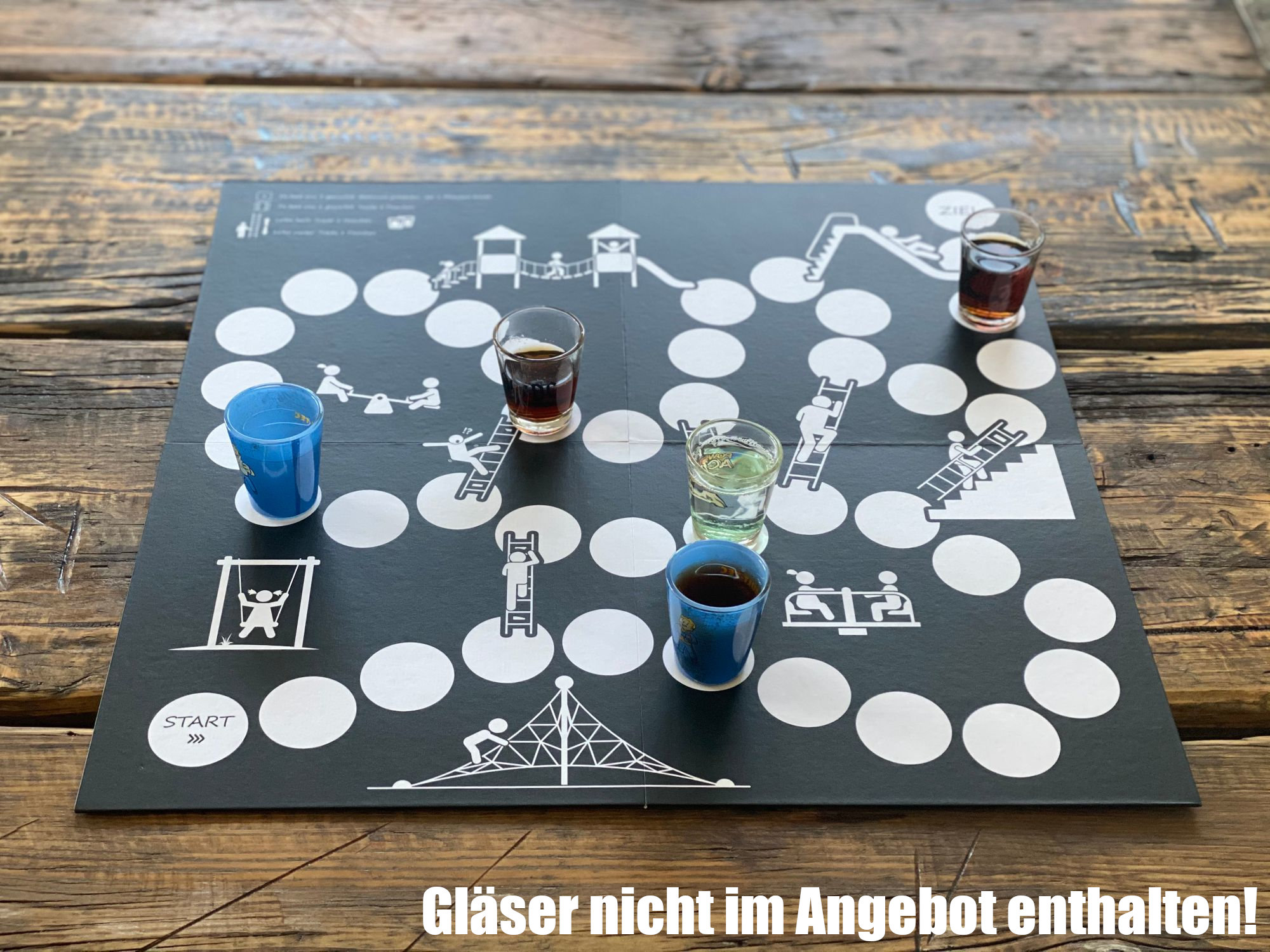 Ein Brettspiel mit Schnapsgläsern auf einem Holztisch. Der Text darunter lautet: Gläser nicht enthalten!