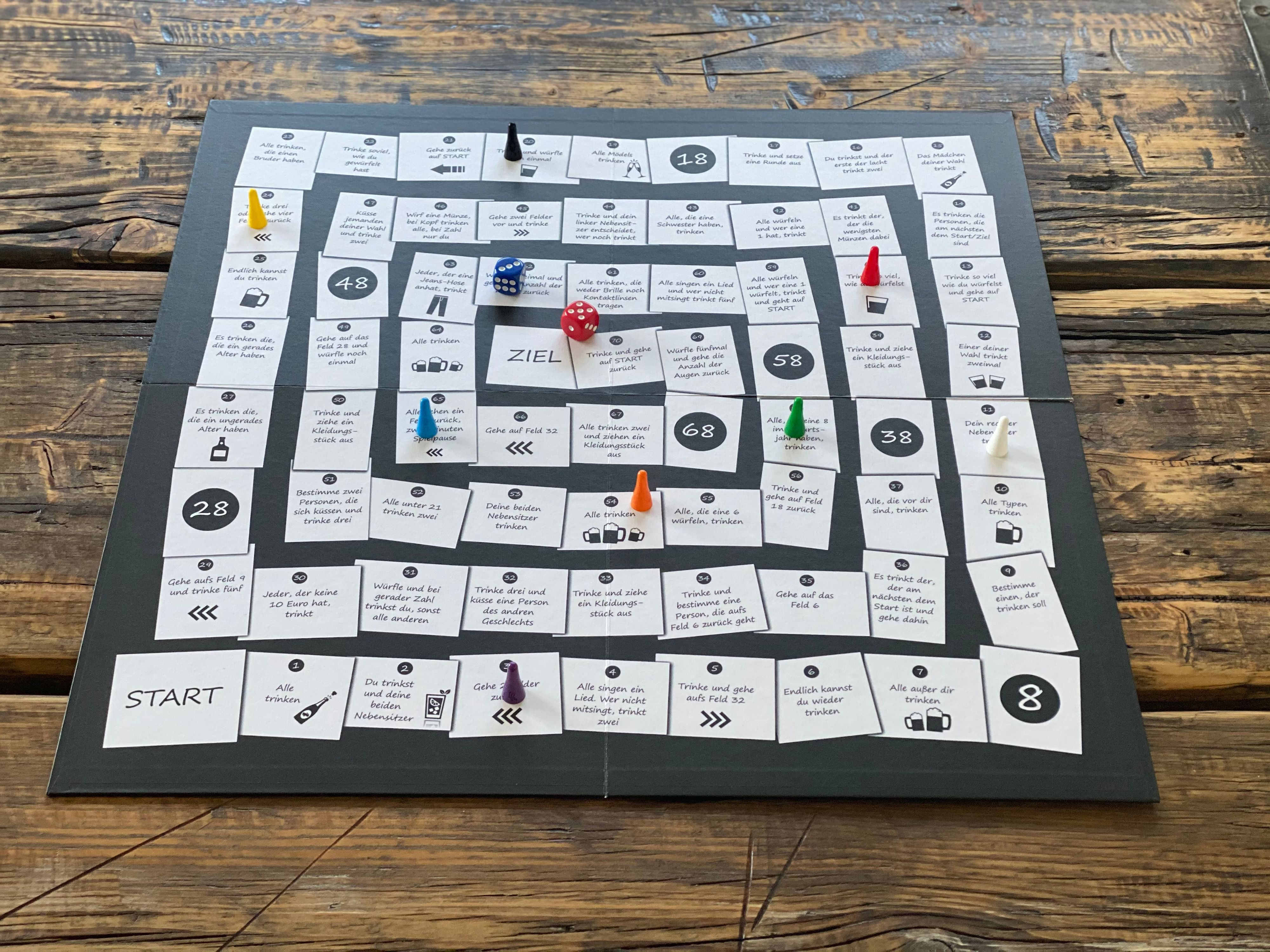 Brettspiel auf einem Holztisch, mit Würfeln, Spielfiguren und Anweisungen auf Deutsch.
