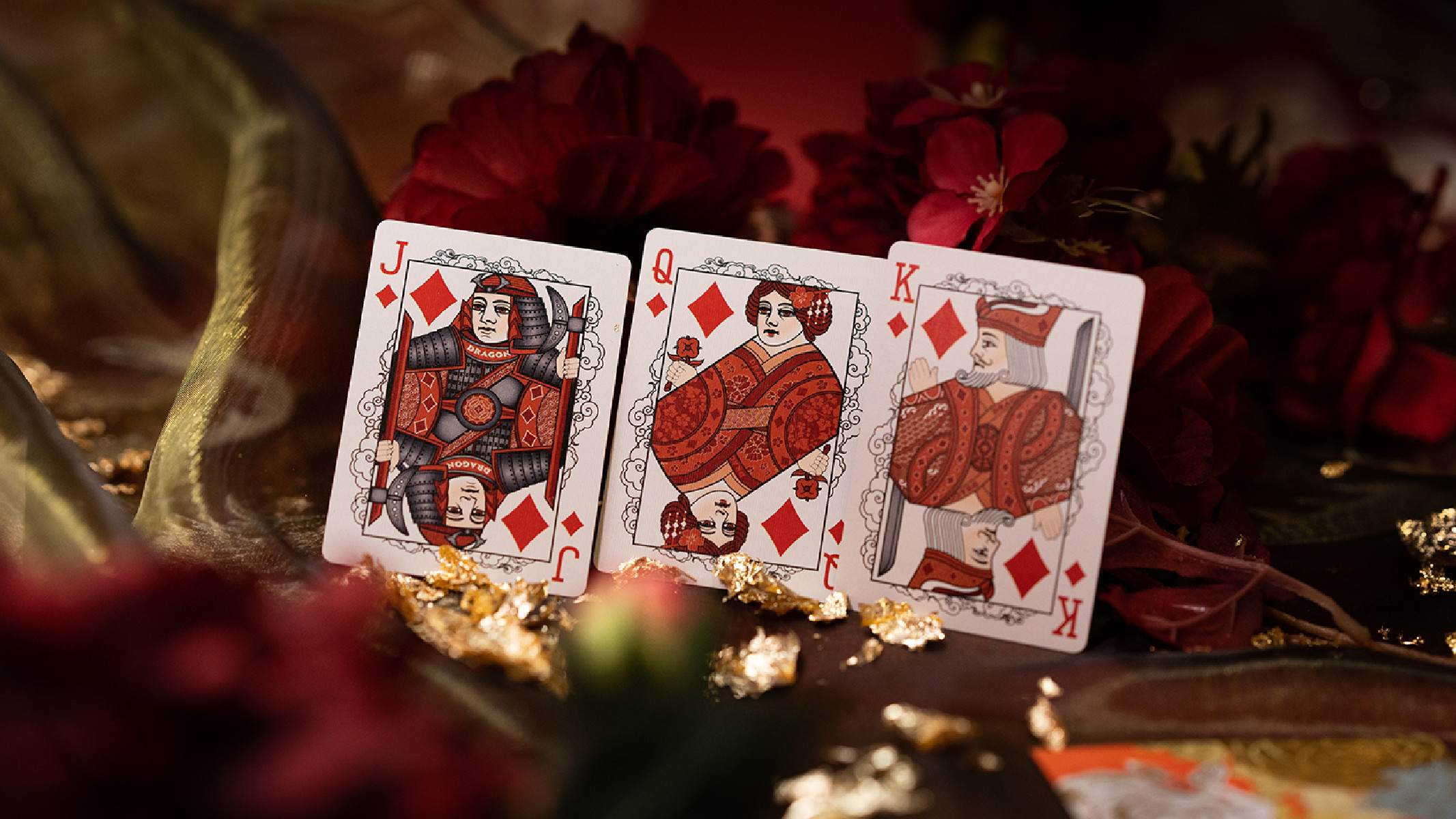Spielkarten: Bube, Dame und König Karo, auf rotem floralen Hintergrund.