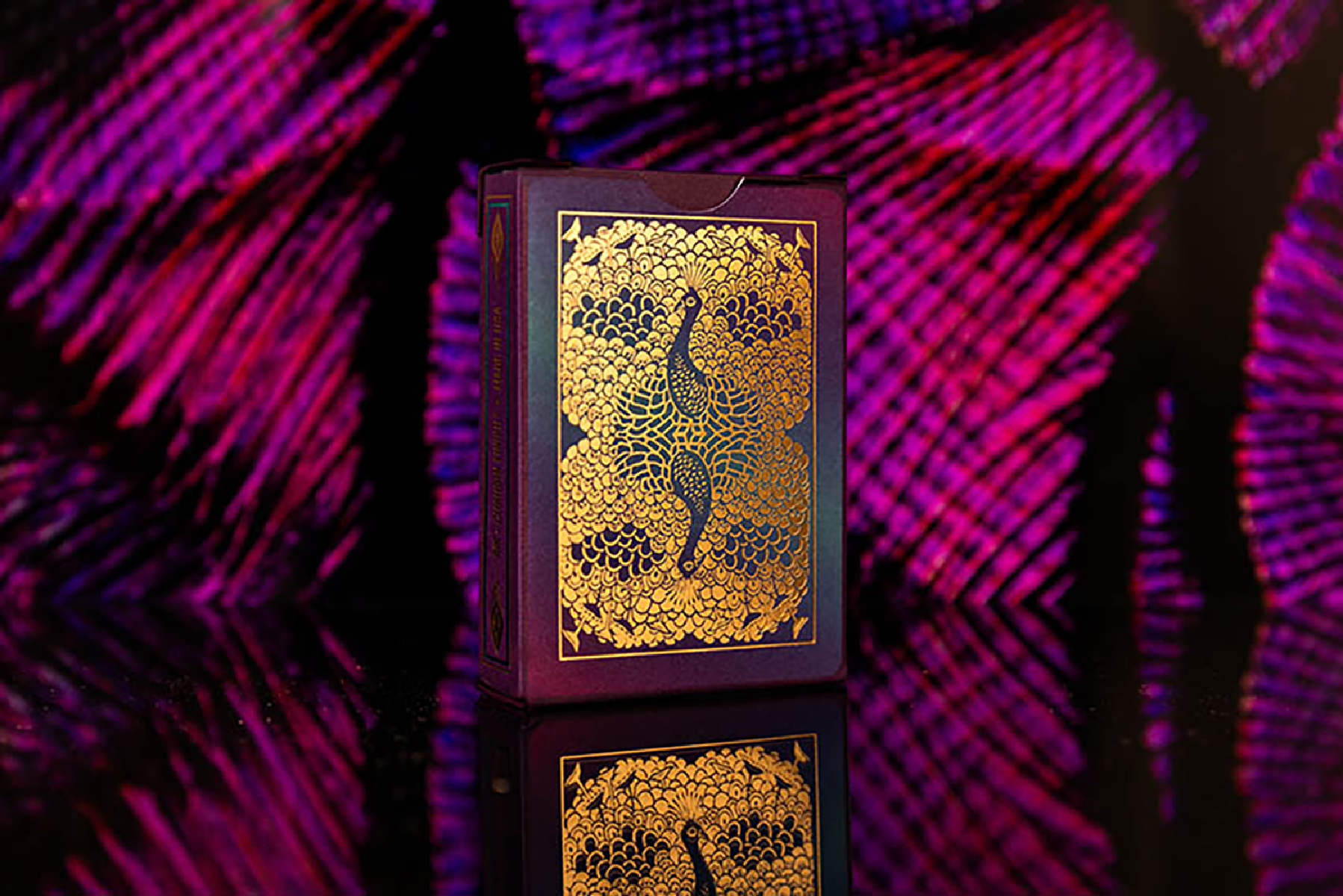 Eine Spielkartenbox mit goldenem Pfauendesign auf einem lila Hintergrund.
