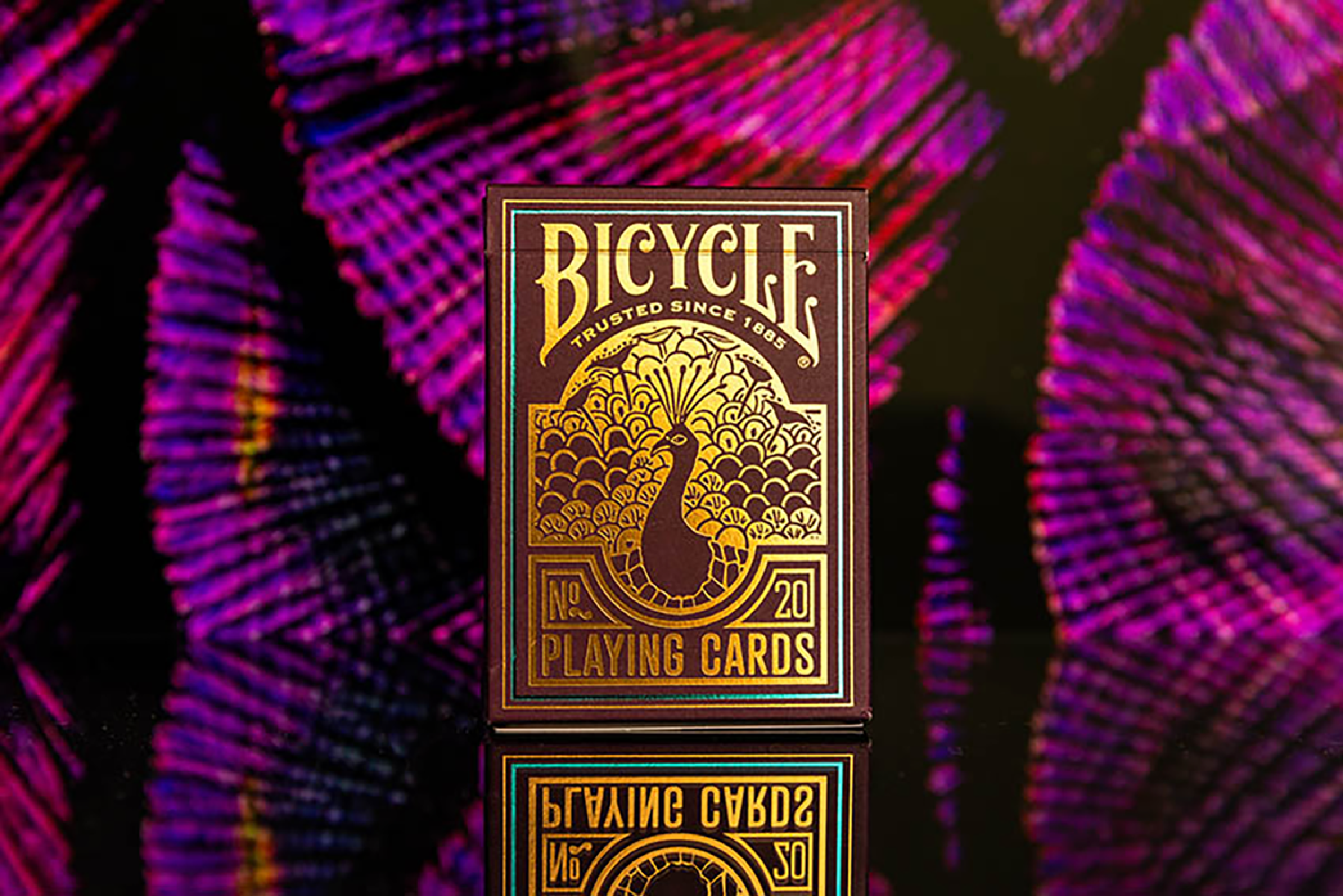 Bicycle Spielkartenbox. Die Box ist dunkelbraun mit goldenem Pfau und Text auf lila Hintergrund.