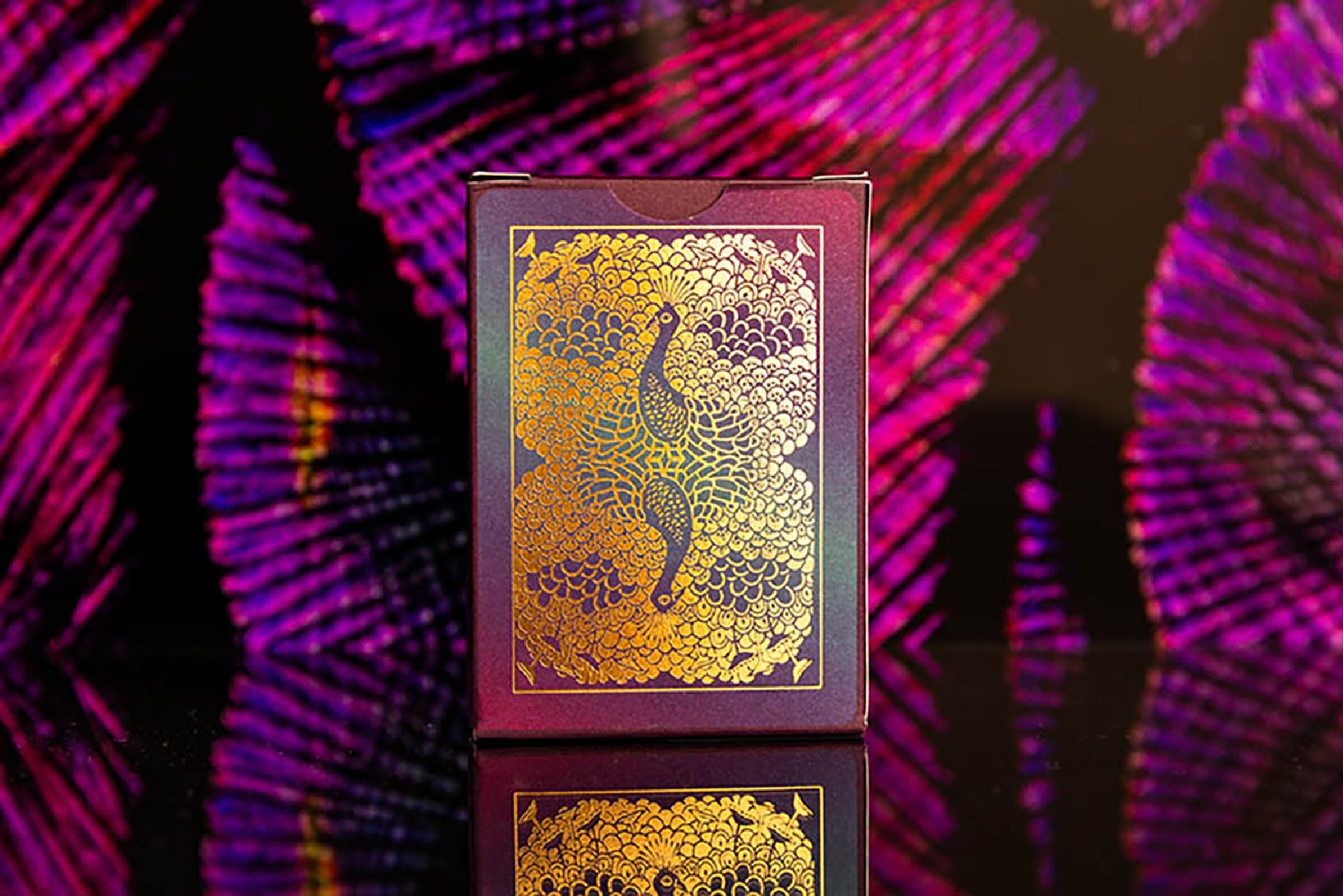 Spielkartenbox mit goldenem Pfauendesign auf lila Hintergrund.