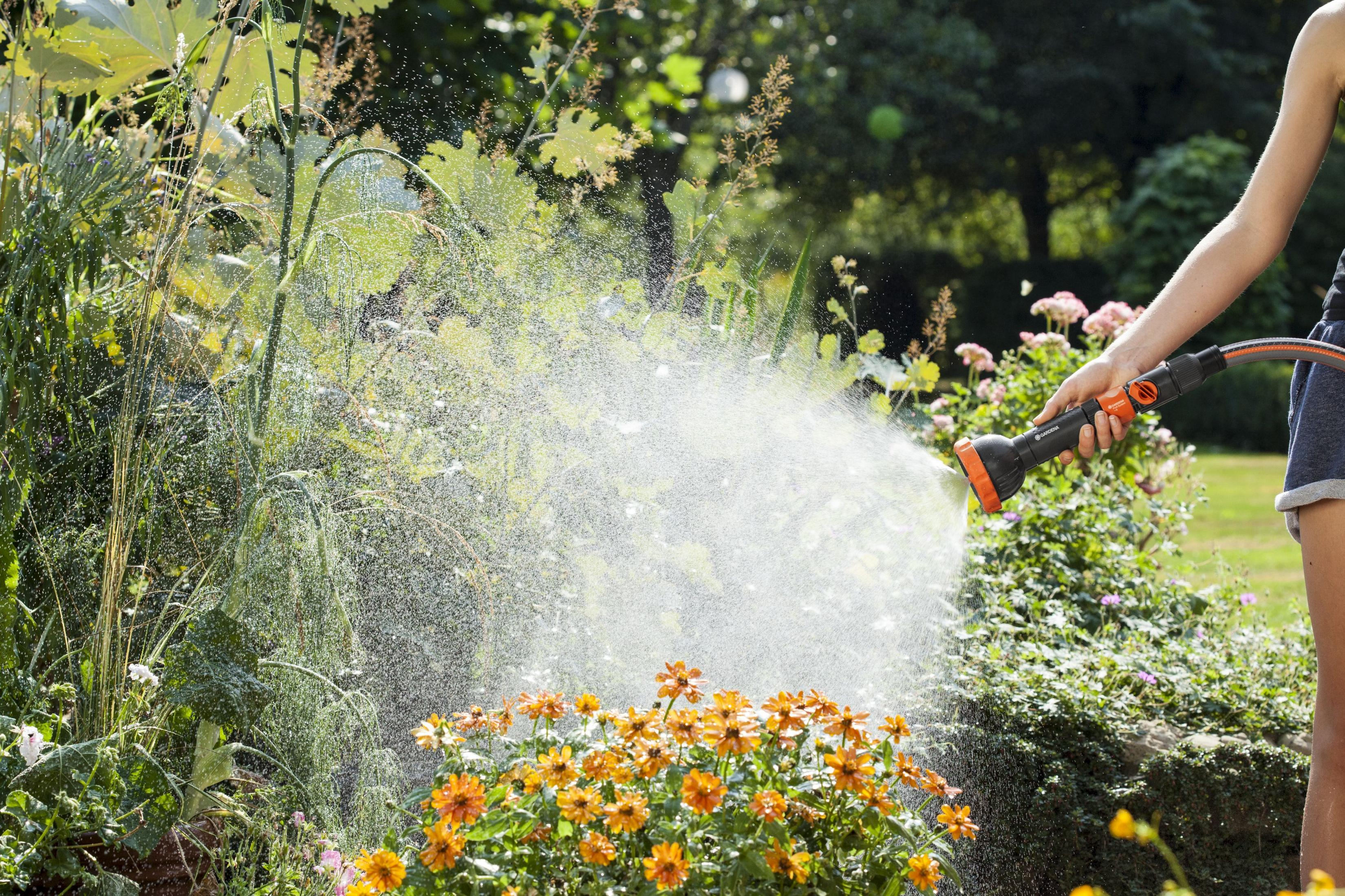 Persona che innaffia fiori con un ugello Gardena in giardino.