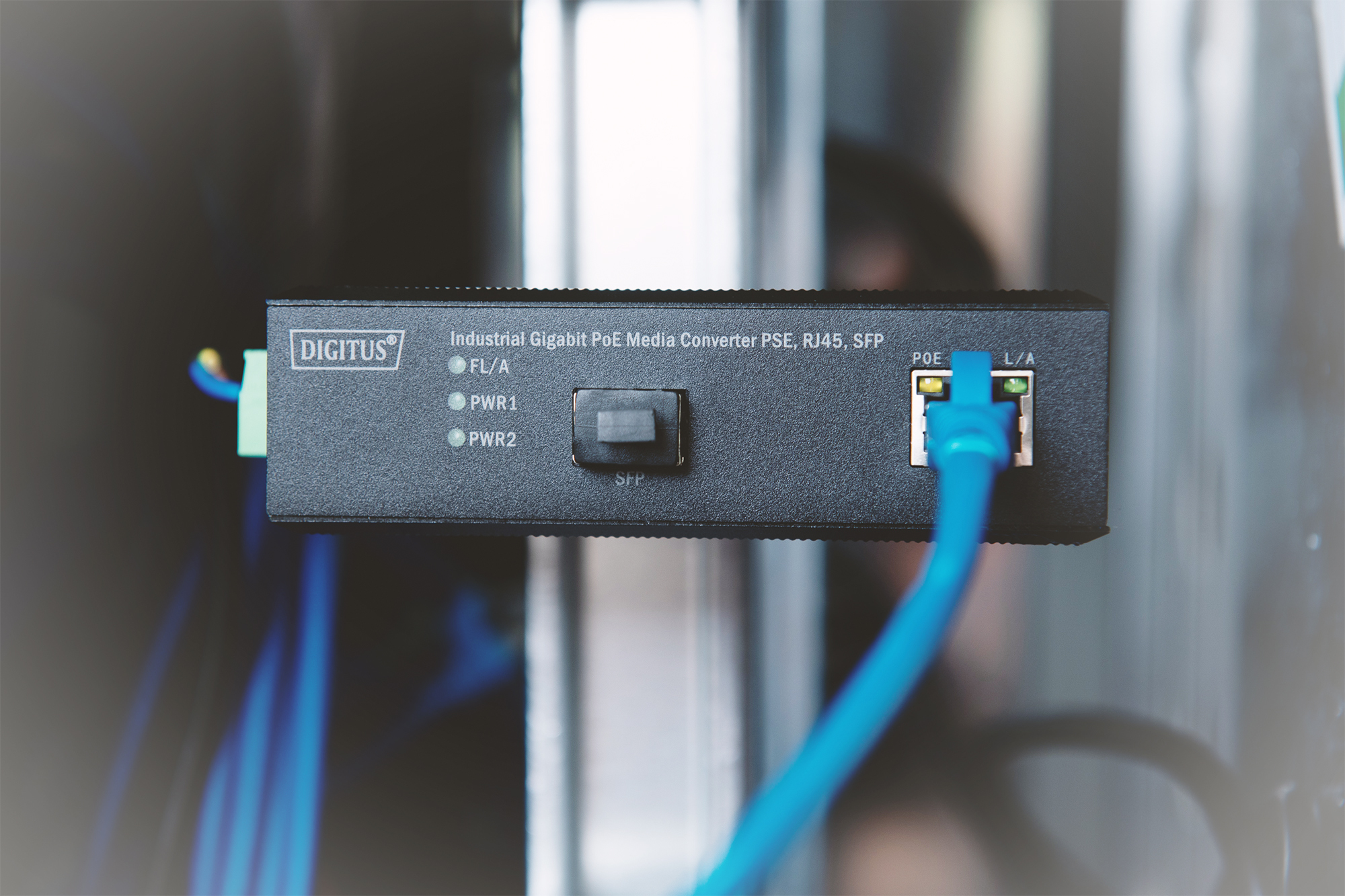Czarne urządzenie sieciowe z niebieskim kablem. Napis: 'DIGITUS Industrial Gigabit PoE Media Converter'.