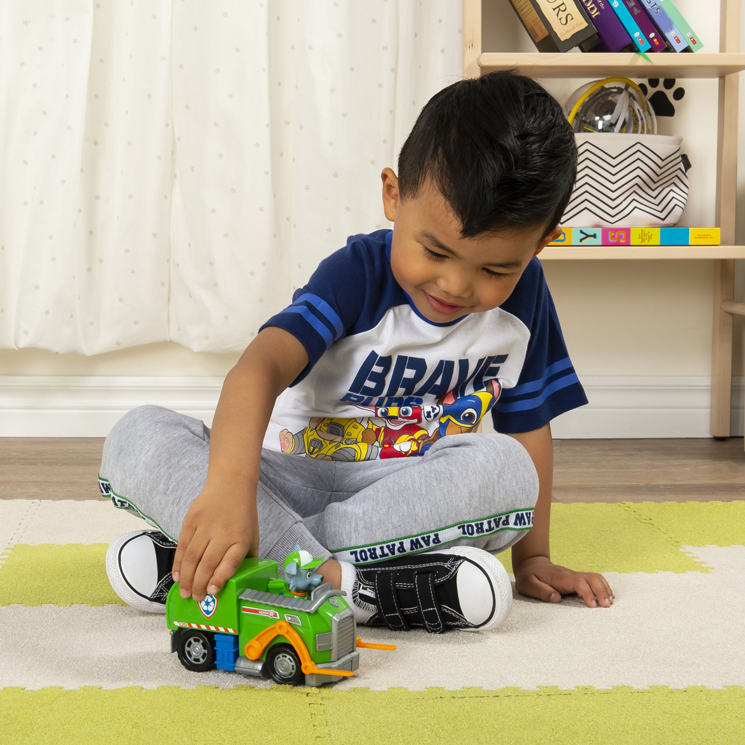Niño jugando con un camión verde de Paw Patrol en una alfombra colorida.