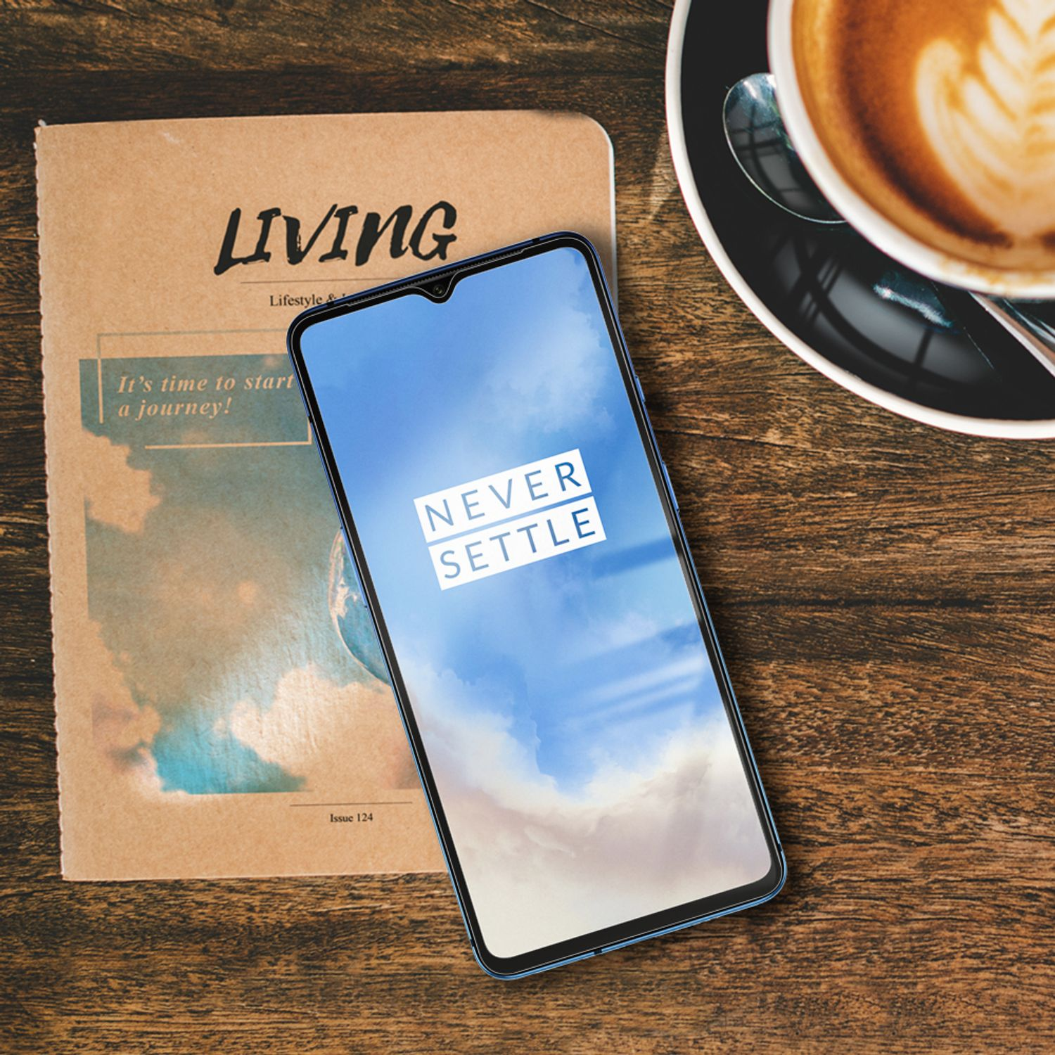 Téléphone avec un écran bleu, le texte : Never Settle, sur une table en bois avec un magazine.