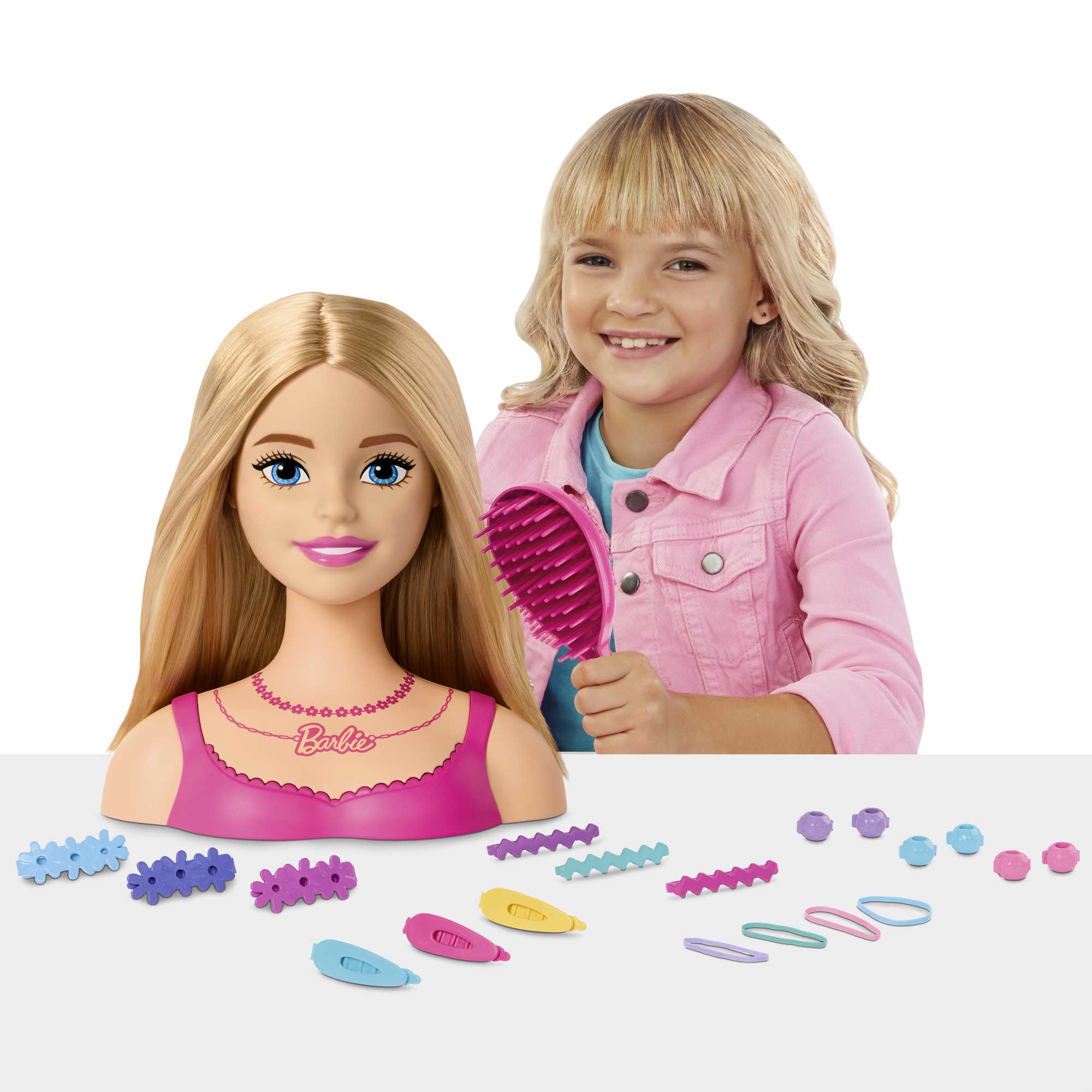 Dziewczynka i głowa do stylizacji Barbie z różową szczotką i akcesoriami. Widoczne liczne spinki do włosów.