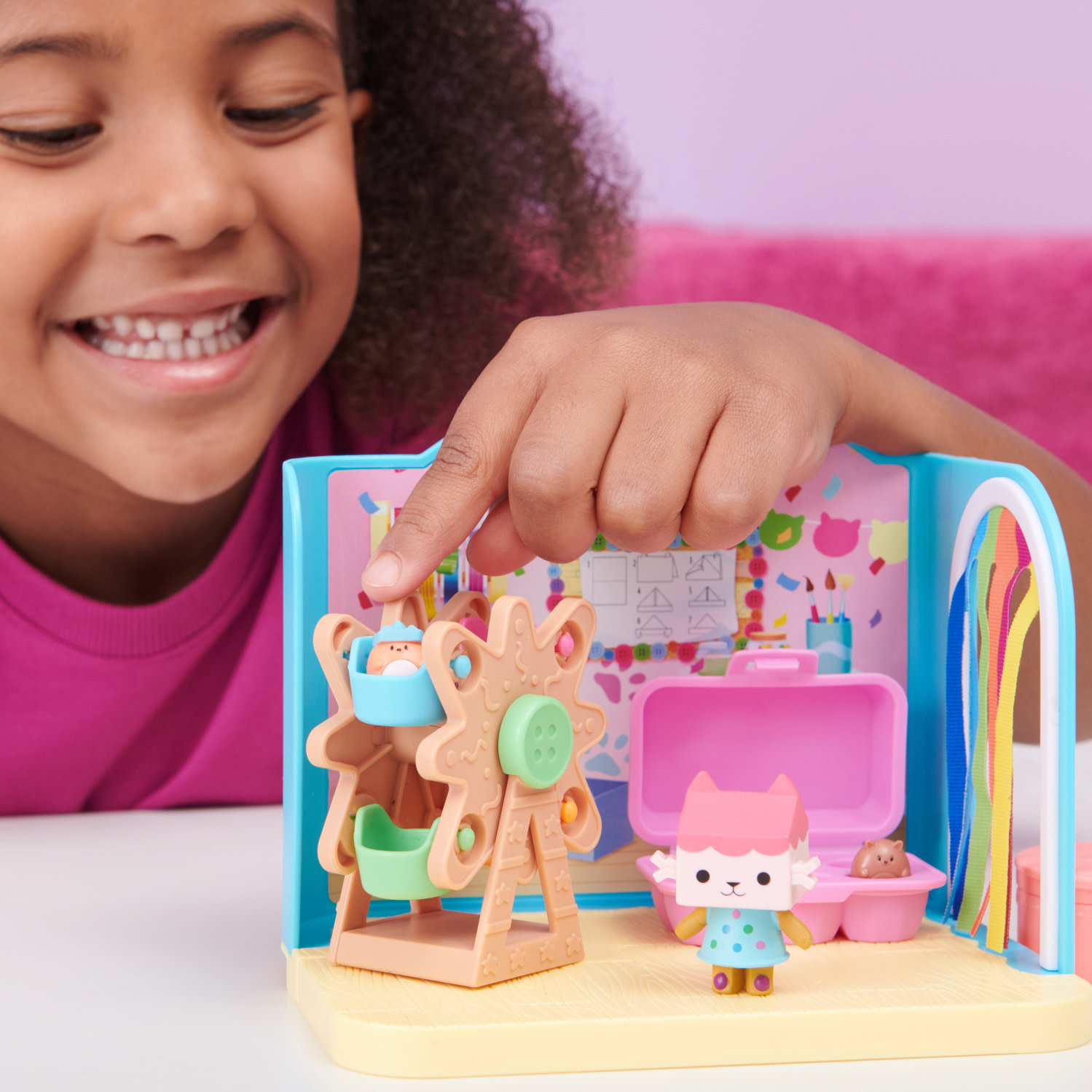 Ein Mädchen zeigt auf ein Spielzeug-Riesenrad und andere Spielzeugelemente in einem Spielset mit einer Katzenfigur.