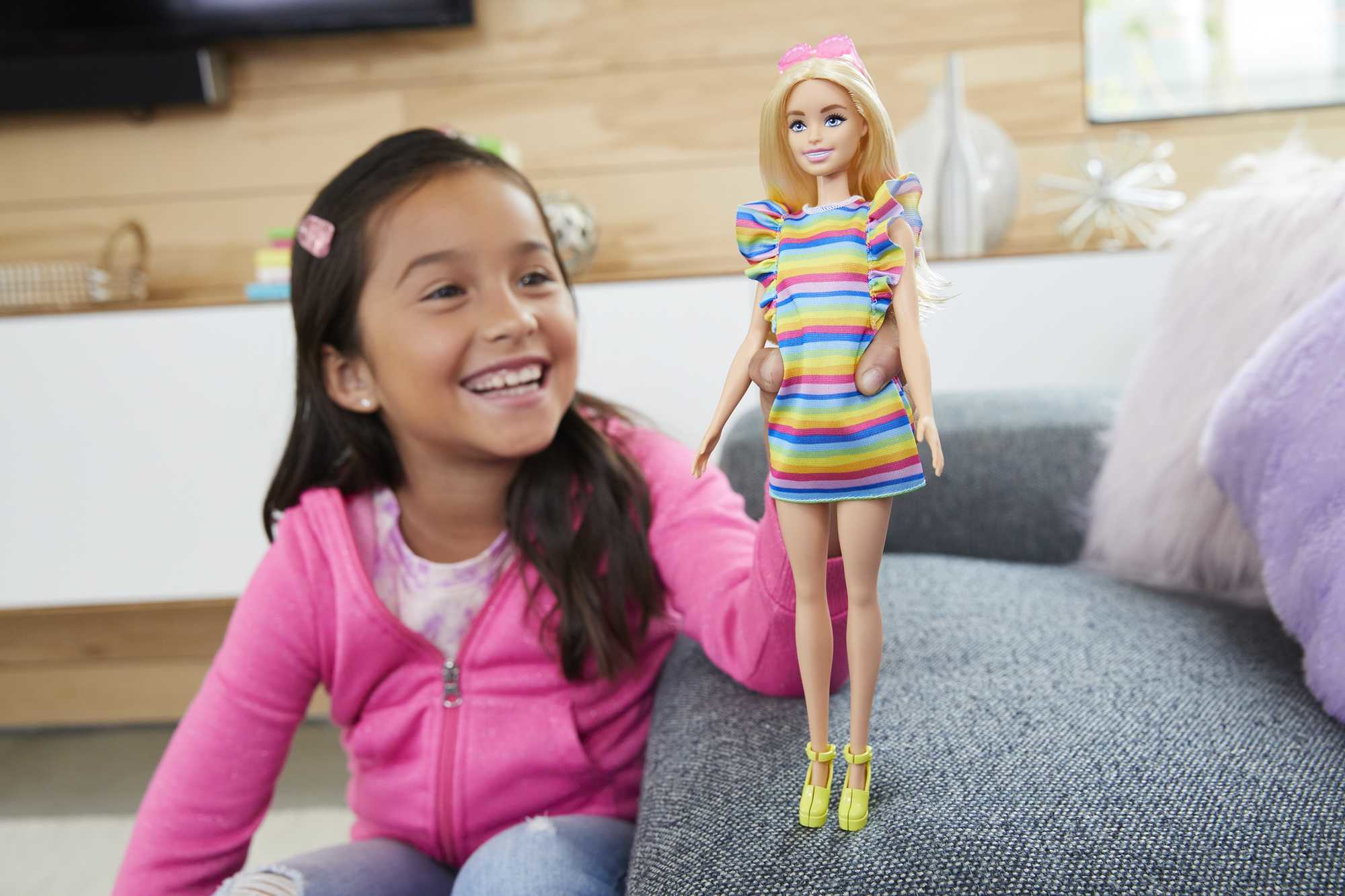 Ein Mädchen h ält eine Barbie-Puppe. Das Mädchen lächelt und sitzt auf einem Sofa.