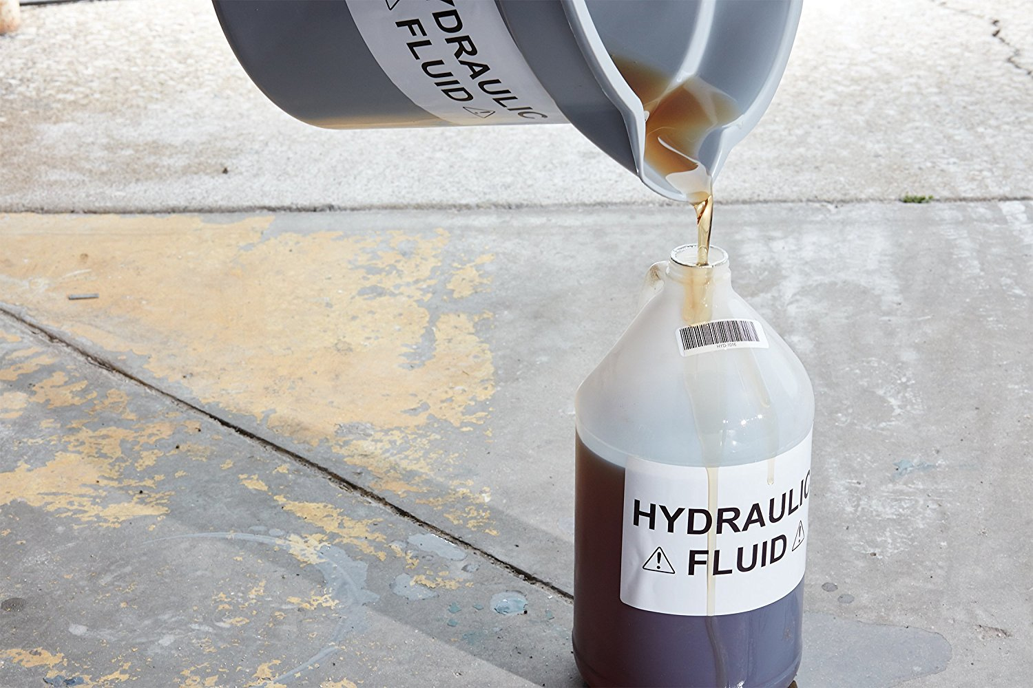 Liquido marrone versa da un beccuccio grigio in un contenitore bianco, con etichette.
