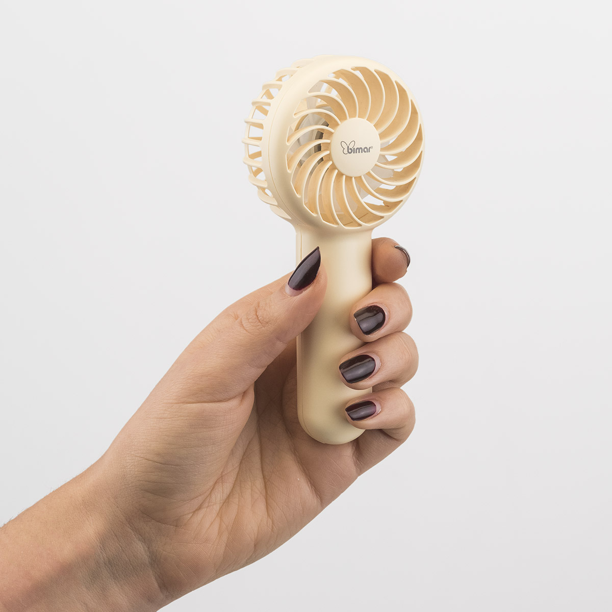 Mano che tiene un ventilatore portatile beige. Pale visibili. Smalto rosso scuro.