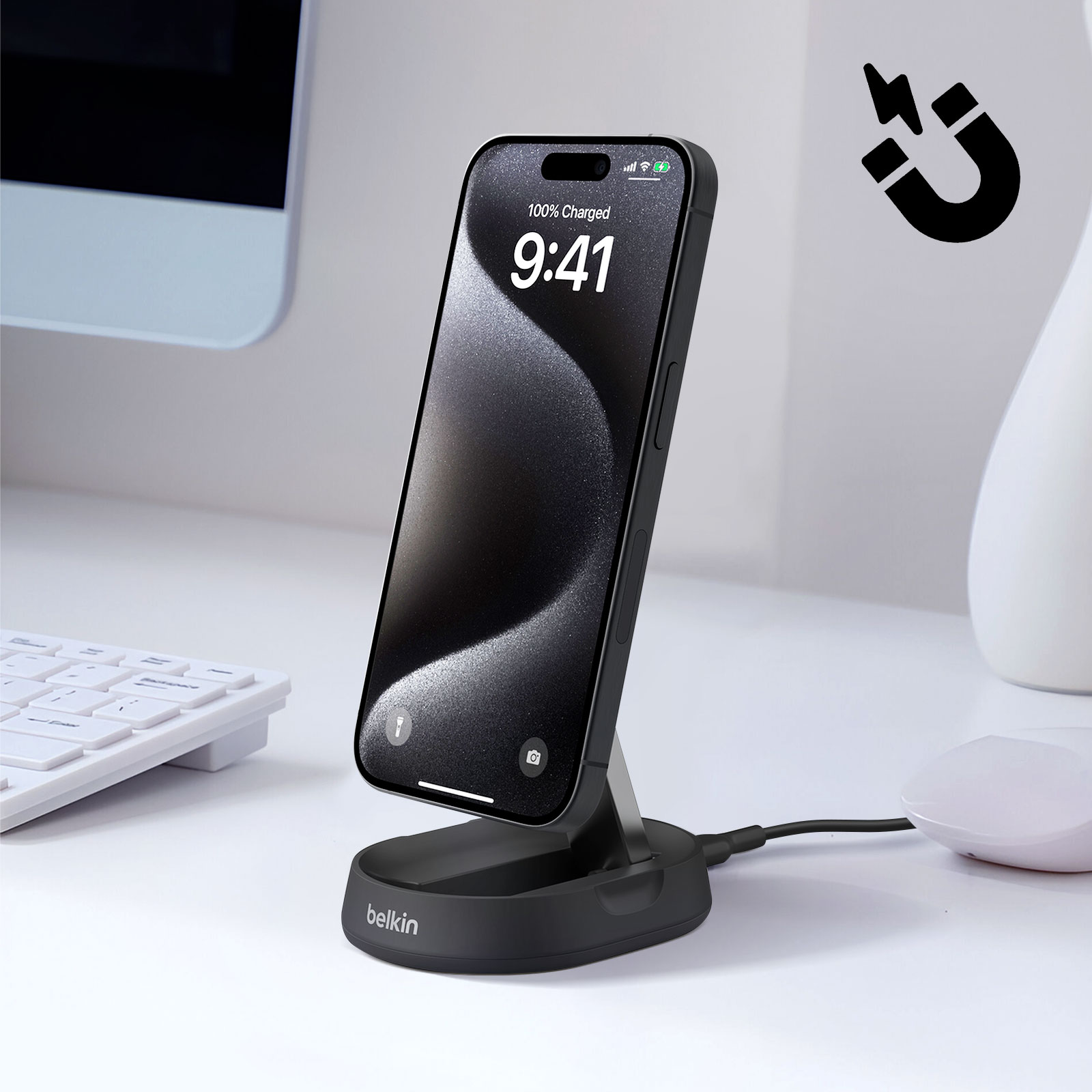 Schwarzes Telefon auf einem Ständer, lädt. Magnet-Symbol rechts. Weißer Schreibtisch, Tastatur und Maus im Hintergrund.