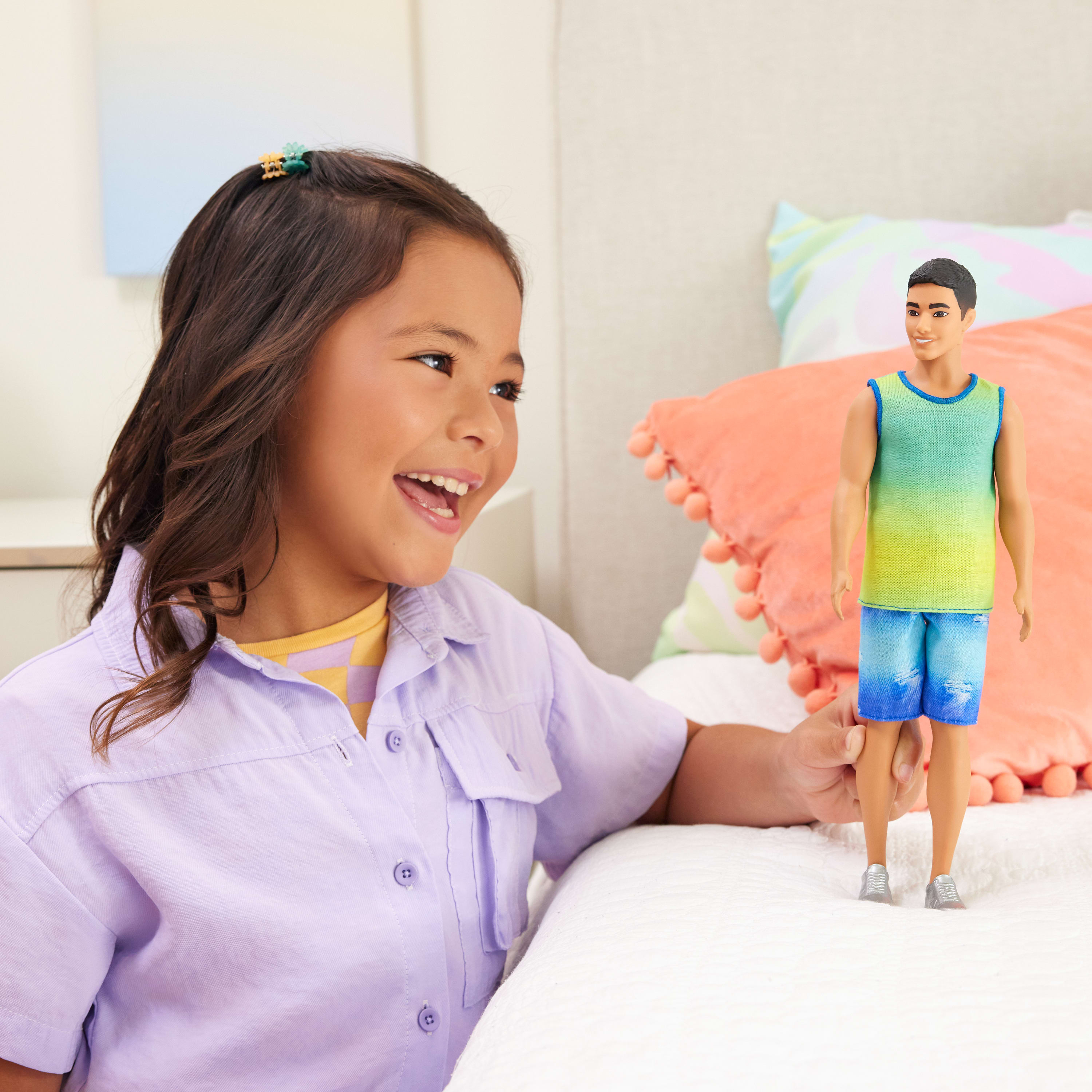 Mała dziewczynka uśmiecha się do lalki mężczyzny w niebieskich spodenkach i zielonej koszulce.