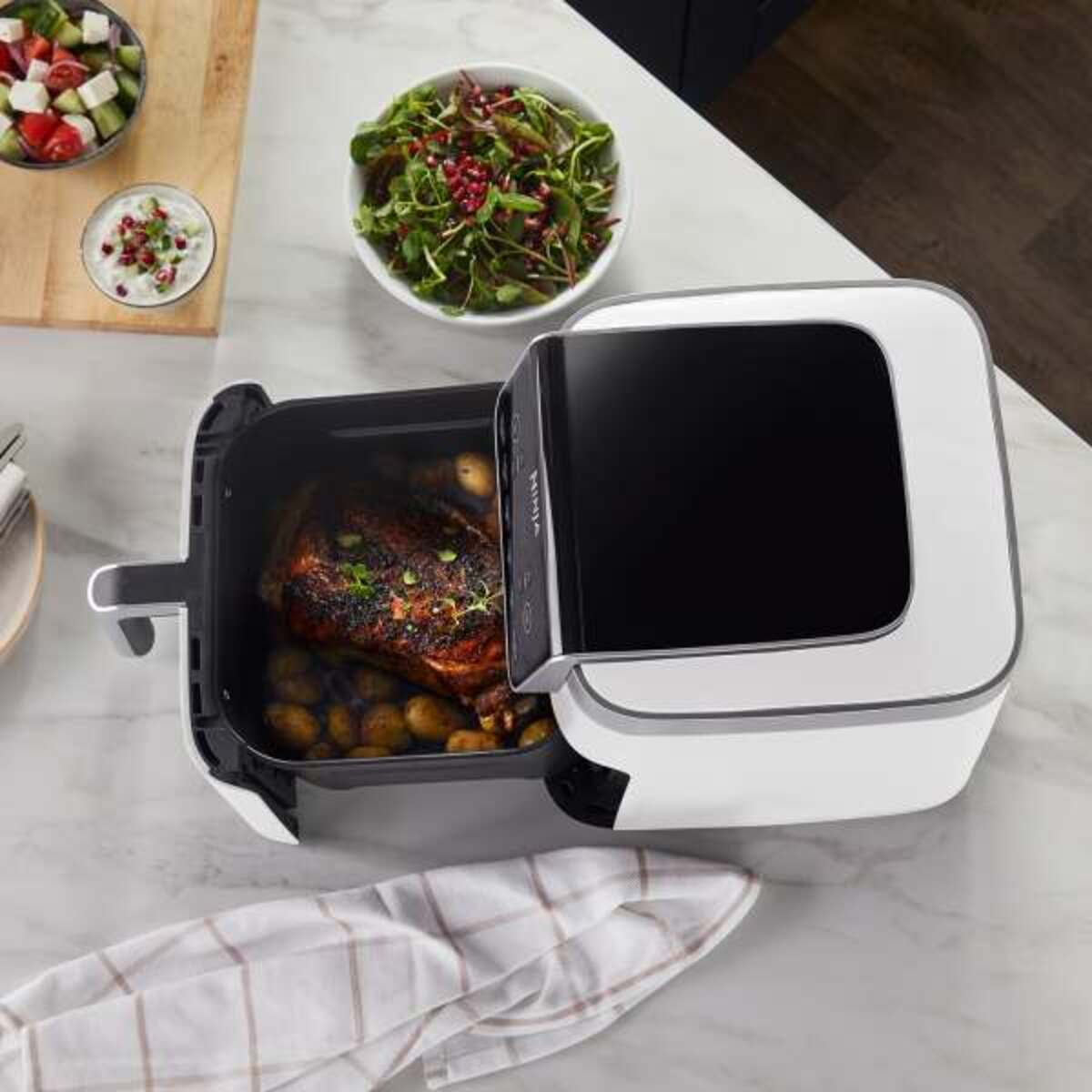 Jedzenie w białej frytkownicy beztłuszczowej. Sałatka i danie z mięsem i ziemniakami. Białe tło.