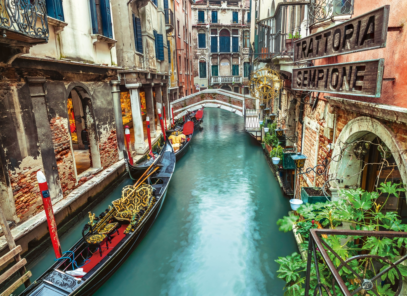 Scène de canal de Venise avec des gondoles, des bâtiments et un pont. Un panneau de trattoria est visible.
