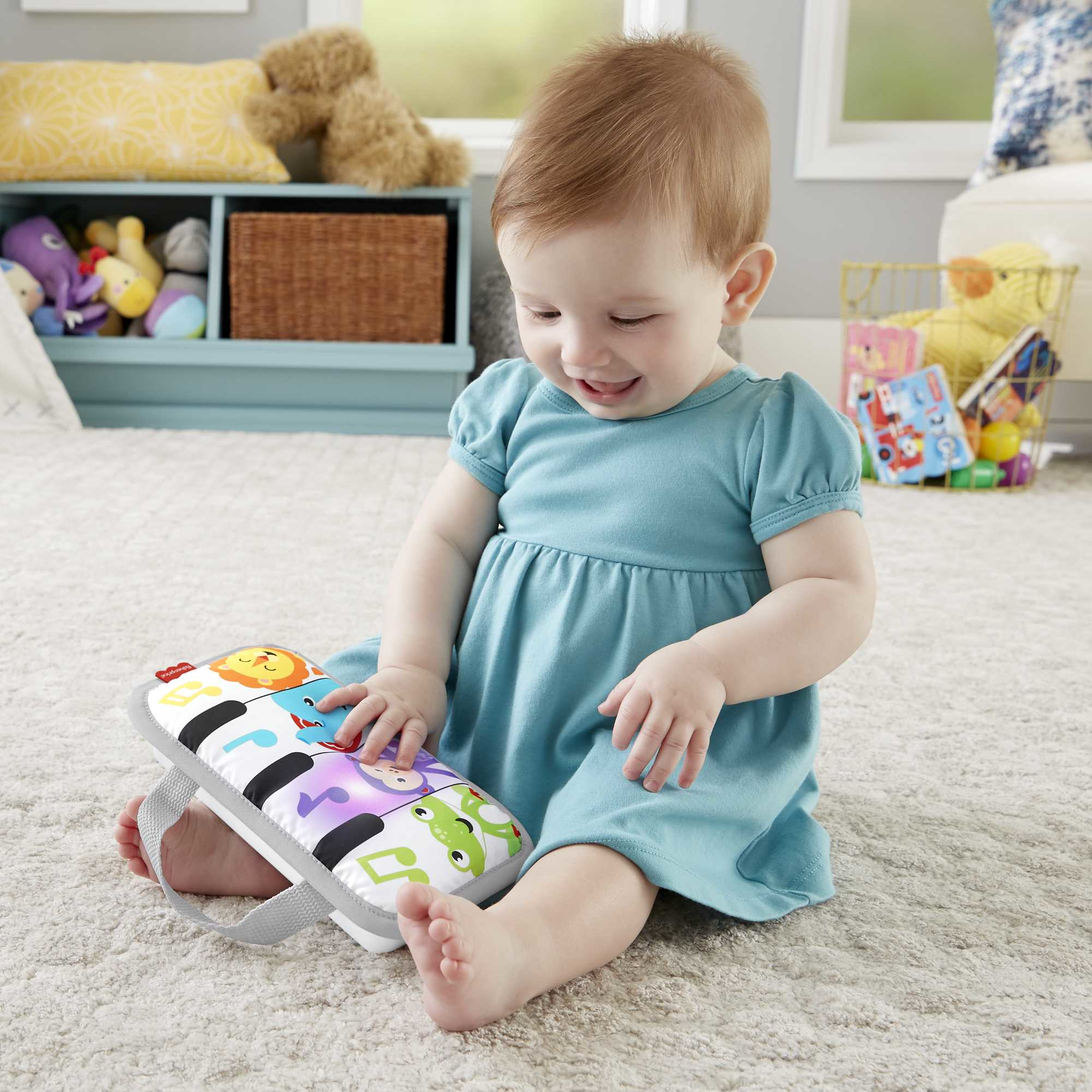 Ein Baby in einem blauen Kleid spielt auf einem Teppichboden mit einem bunten Spielzeugklavier.
