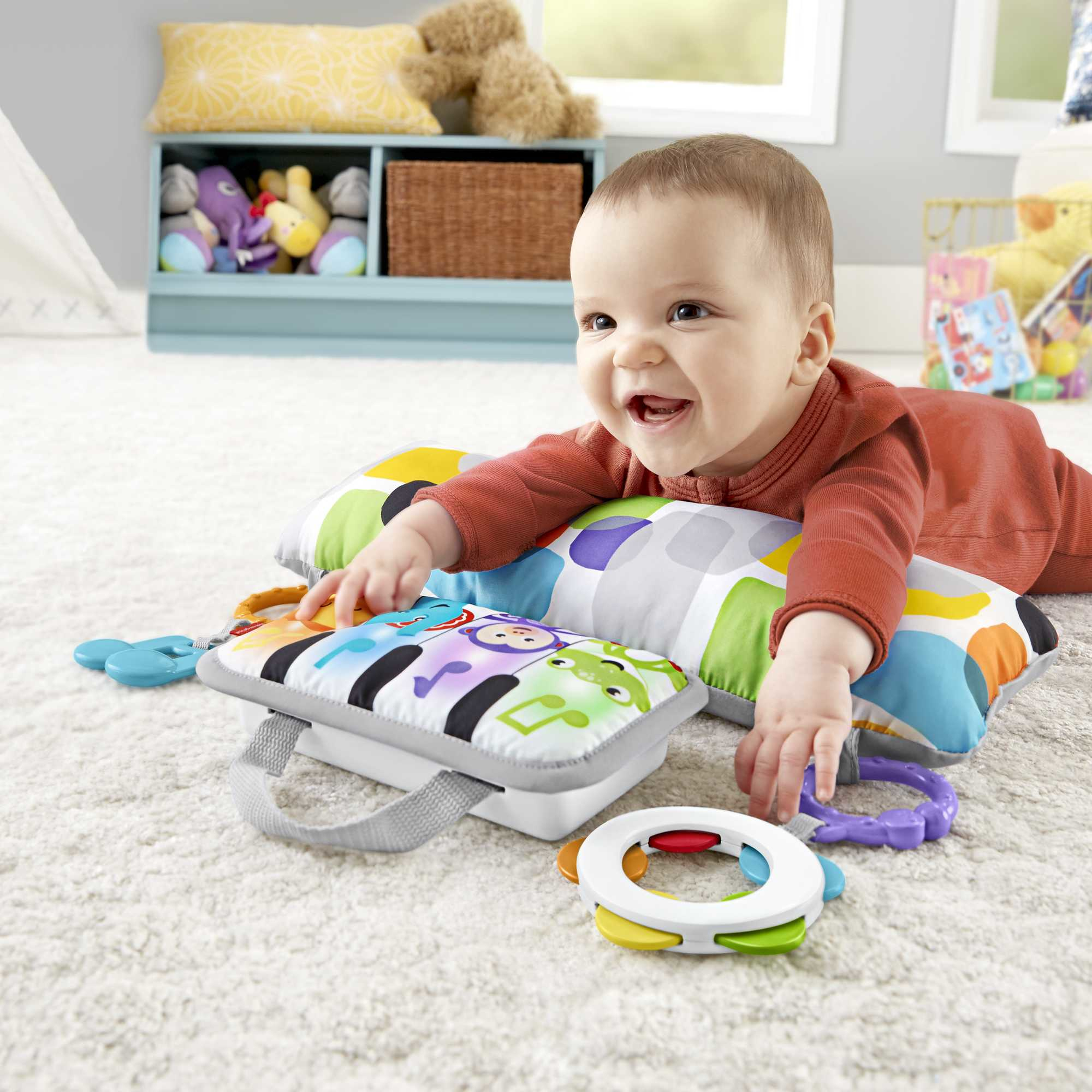 Ein Baby liegt auf einer Spielmatte mit einem Spielzeugklavier und lächelt. Der Hintergrund zeigt Spielzeug auf einem Regal.