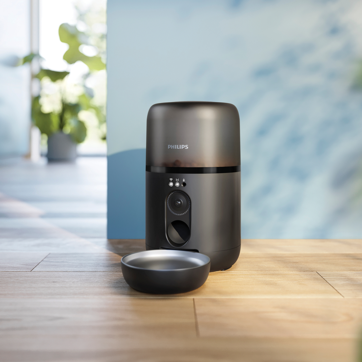 Zwarte en grijze Philips voederautomaat. Het heeft een voerbak. Geplaatst op een houten oppervlak met een vage achtergrond.