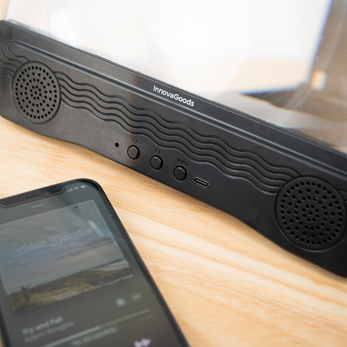 Amplificador de pantalla negro con teléfono sobre mesa de madera. Fondo blanco.