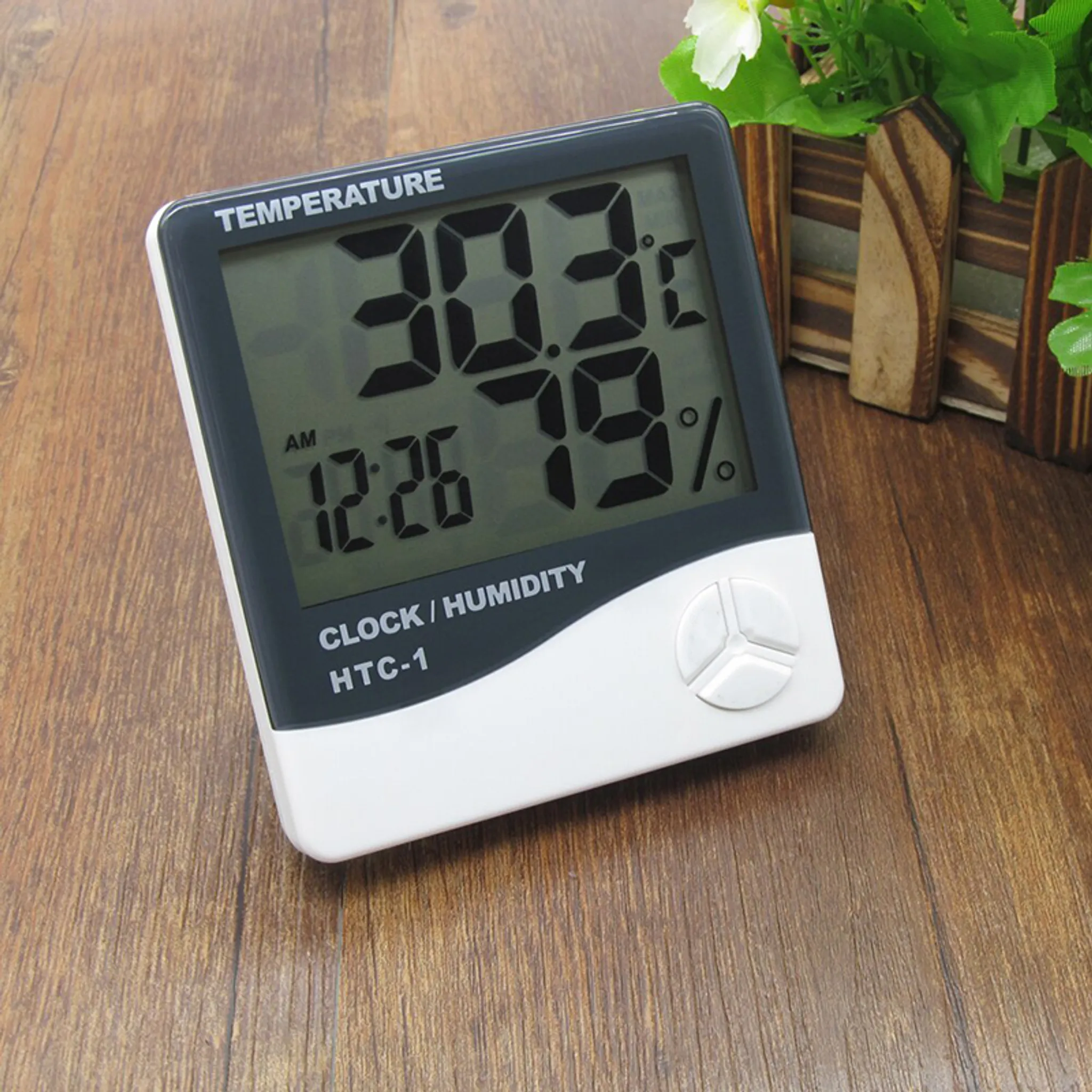 Ein digitales Thermometer zeigt Zeit und Luftfeuchtigkeit an. Das Gerät hat einen weißen und grauen Rahmen.