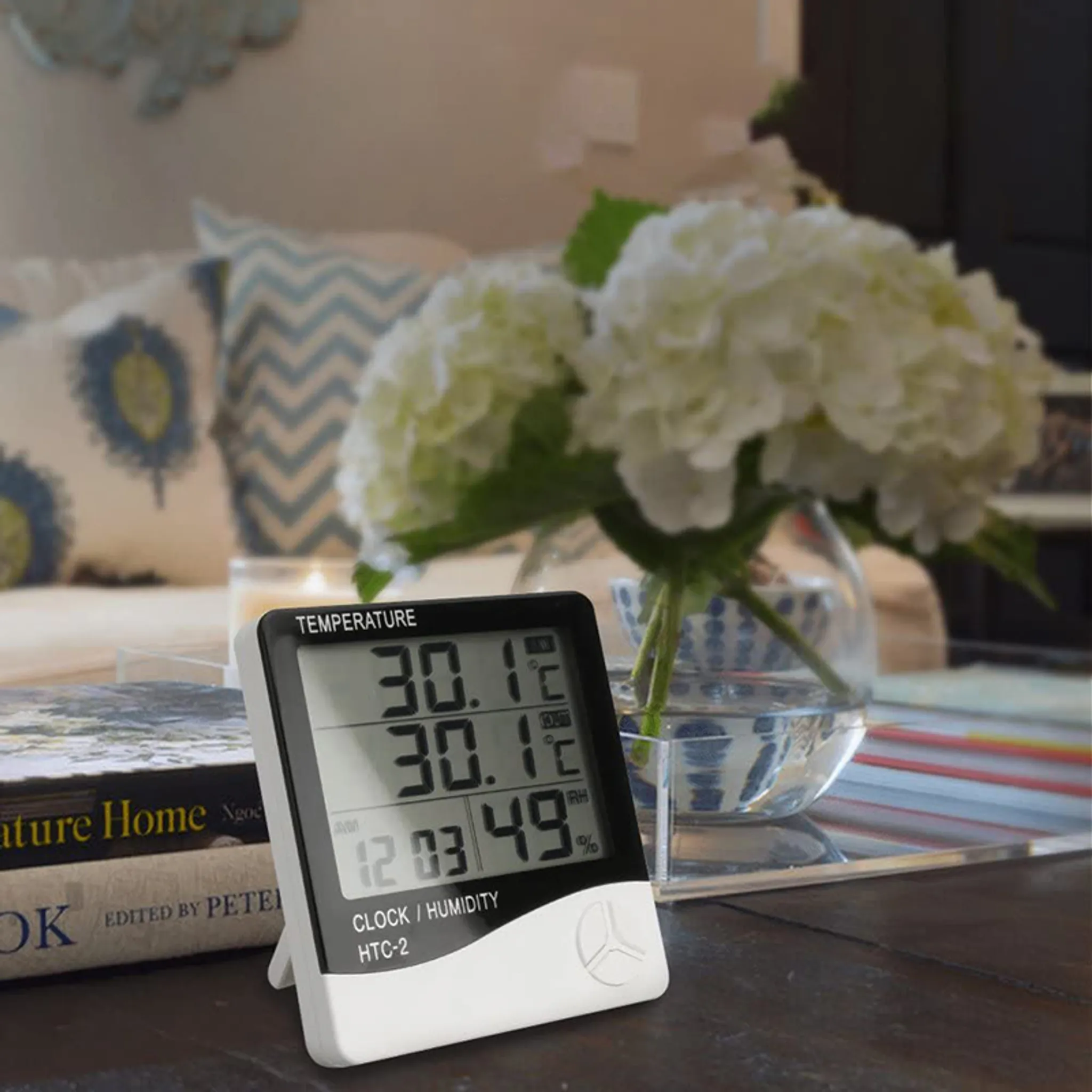 Digitales Thermometer mit einer Vase weißer Blumen im Hintergrund.