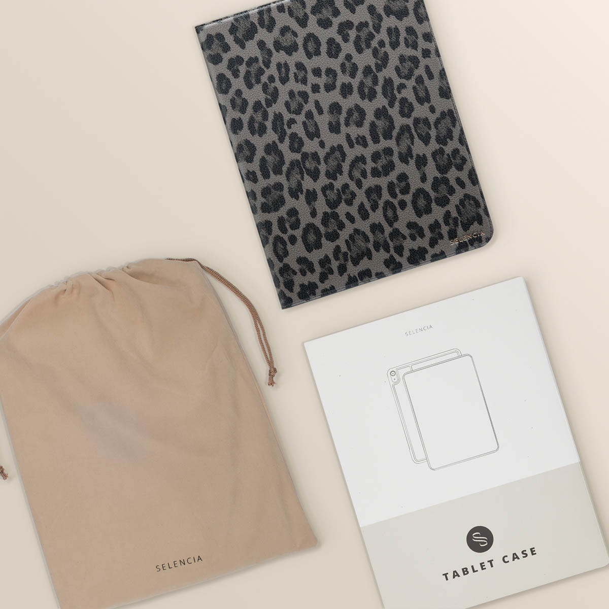 Leopard print tablet case, a beige bag, and packaging on a beige surface.