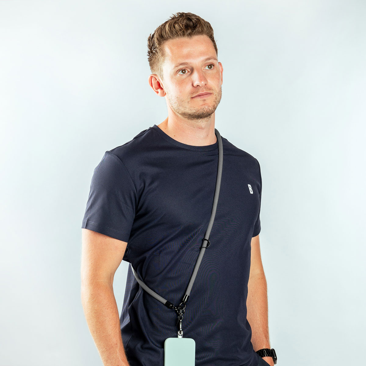 Een man draagt een marineblauw t-shirt met een grijs koord aan een telefoon.