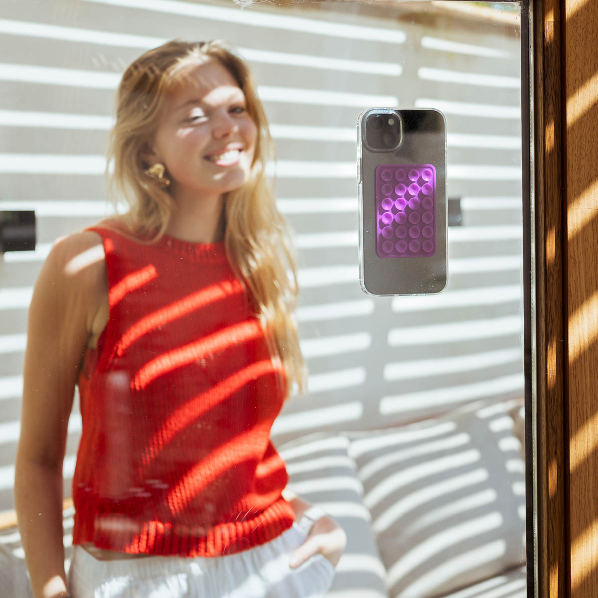 Een vrouw in een rode top, met een telefoon aan het raam bevestigd. De telefoon heeft een paars pop it-speelgoed op de achterkant.