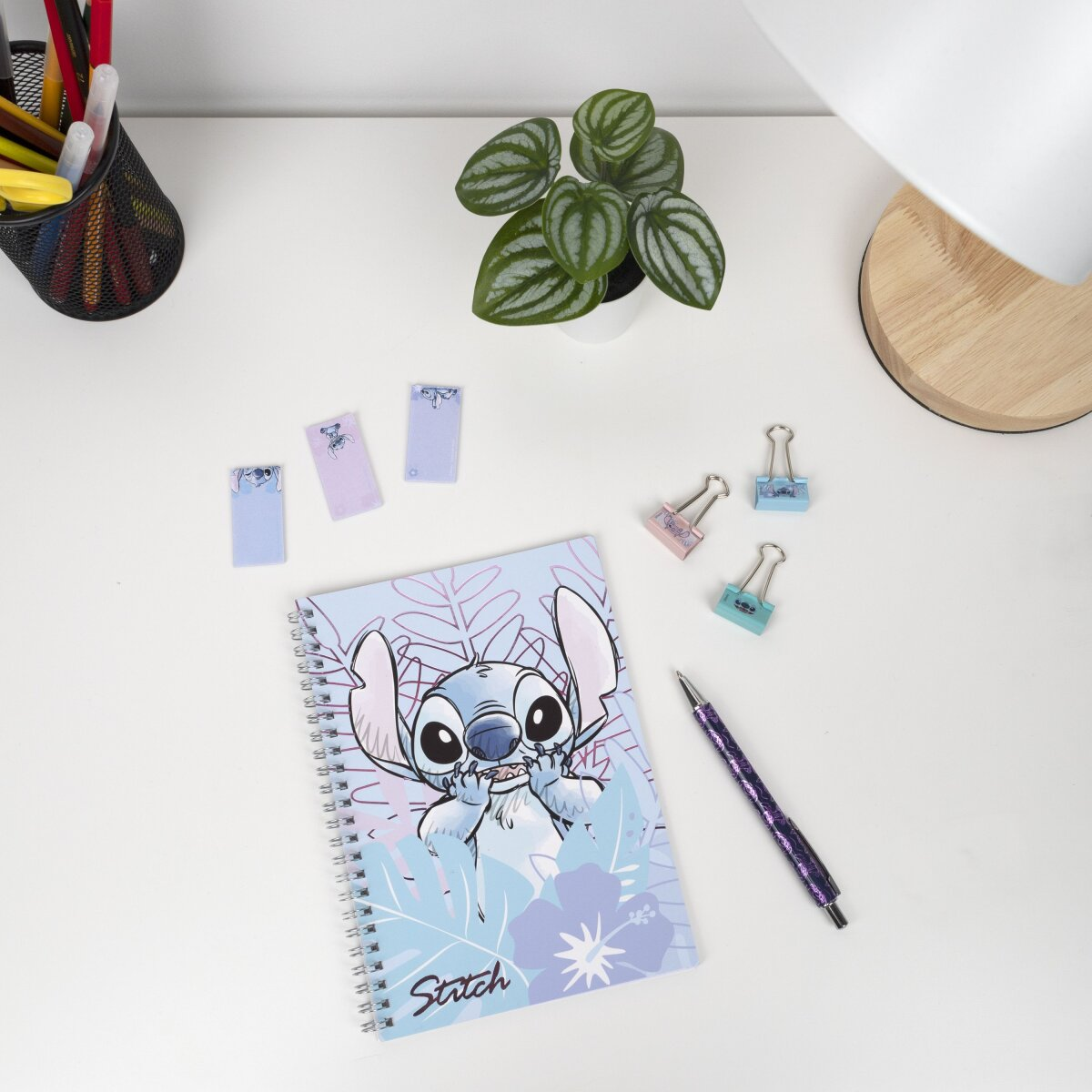 Eine Schreibtischszene mit einem Stitch-Notizbuch, Stift, Haftnotizen, Büroklammern und einer Pflanze.