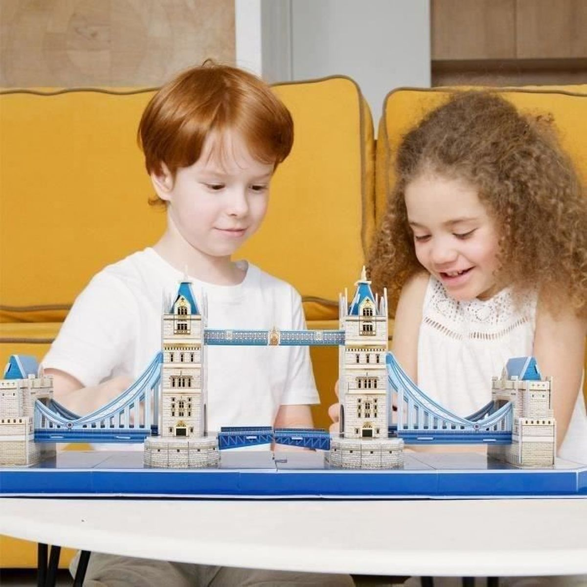 Due bambini che assemblano un puzzle del Tower Bridge. Sfondo del divano giallo. Pezzi del puzzle blu e bianchi.