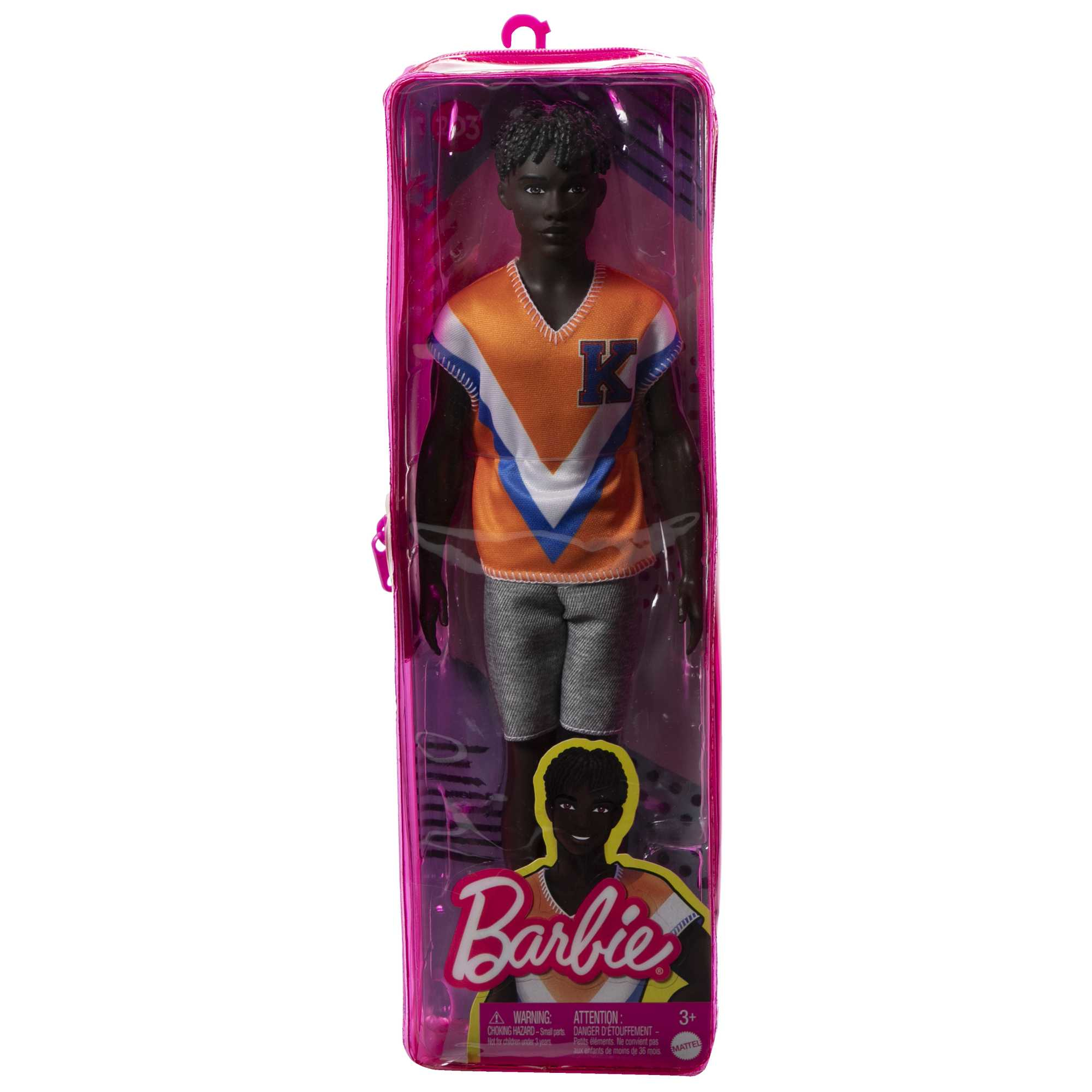 Une poupée noire dans un emballage transparent, portant un haut orange et bleu, un short et des chaussures blanches.