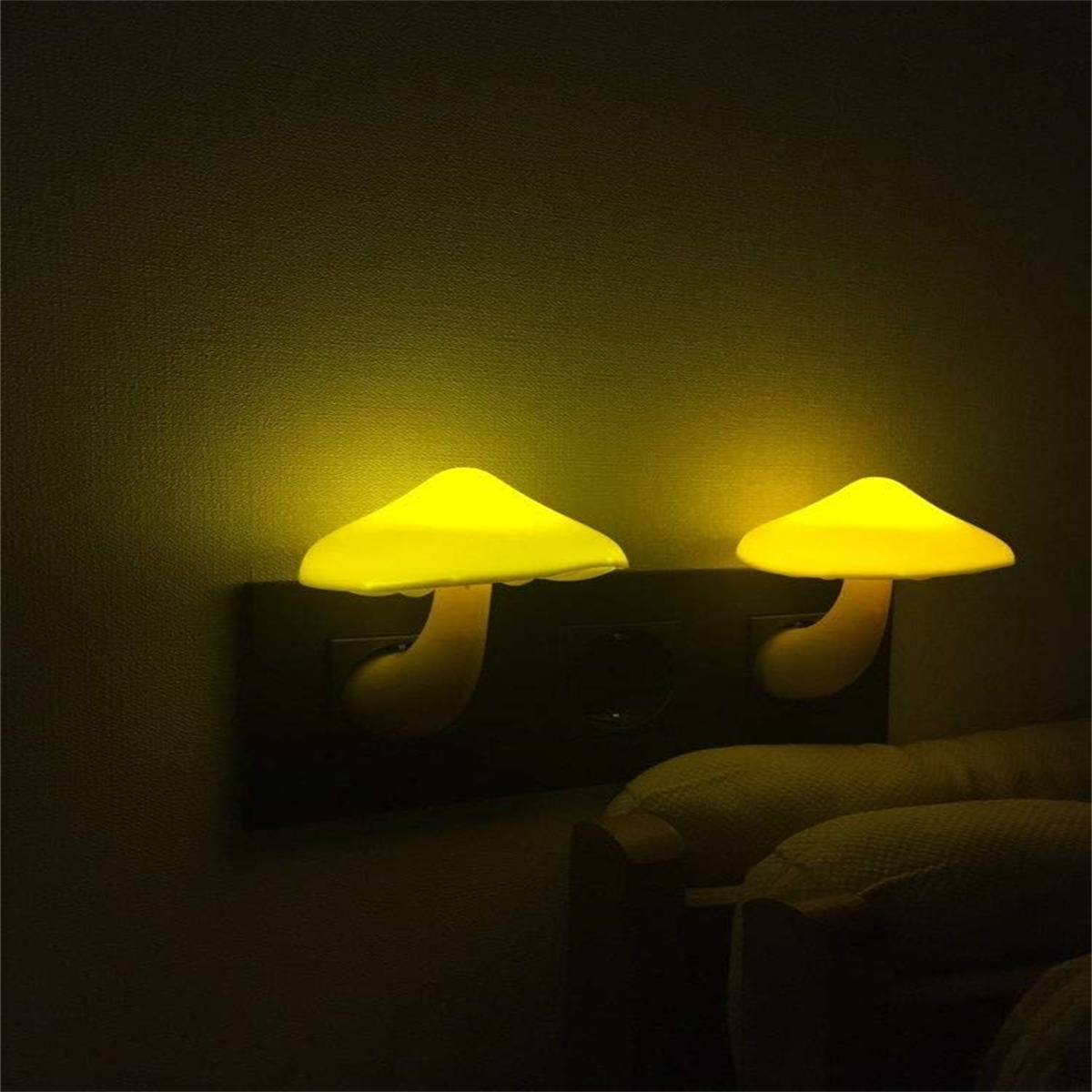 Zwei pilzförmige Nachtlichter an einer Wand. Gelbes Leuchten, montiert auf einer schwarzen Wandplatte.