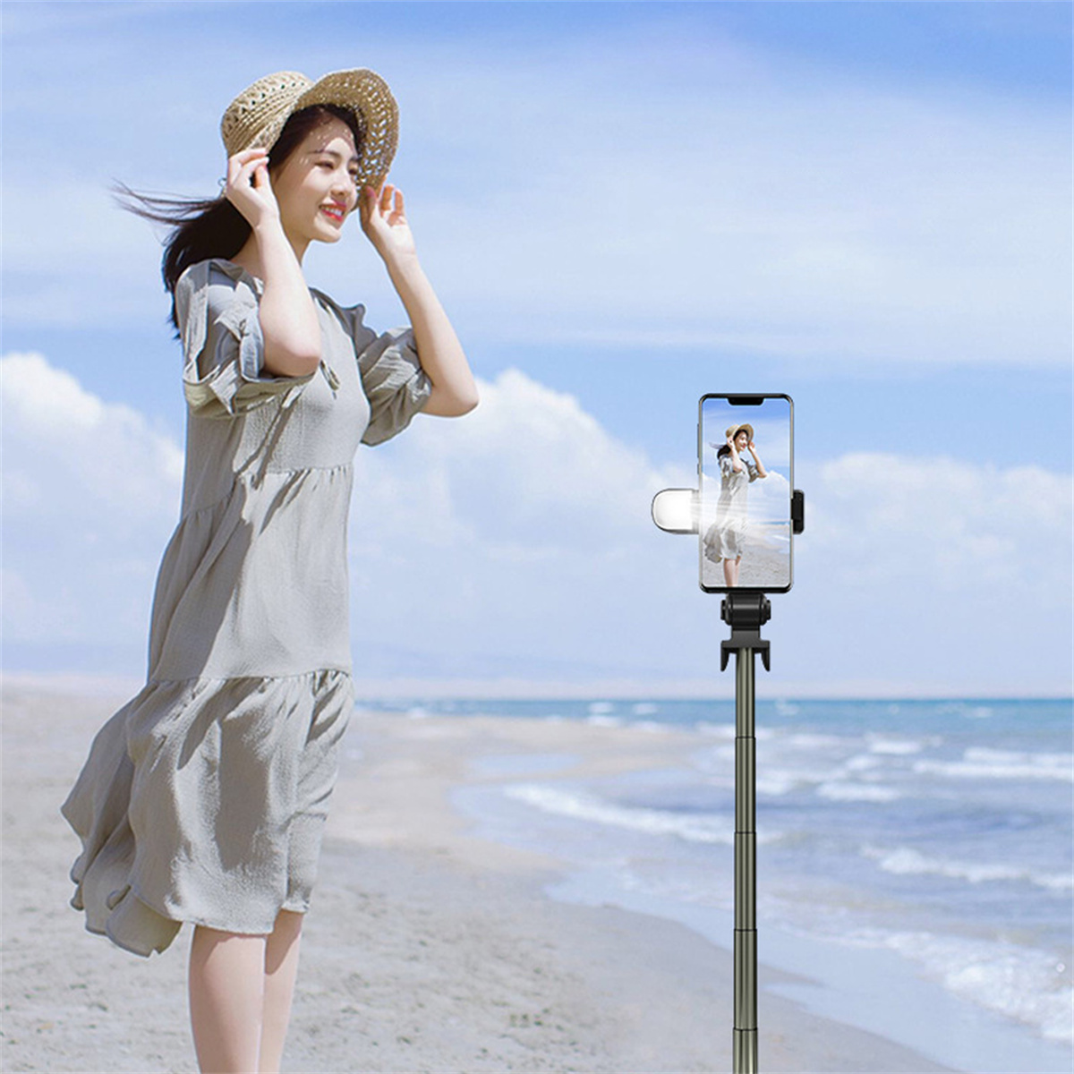 Frau macht Foto mit Telefon auf Selfie-Stick am Strand. Klarer blauer Himmel und Meer.
