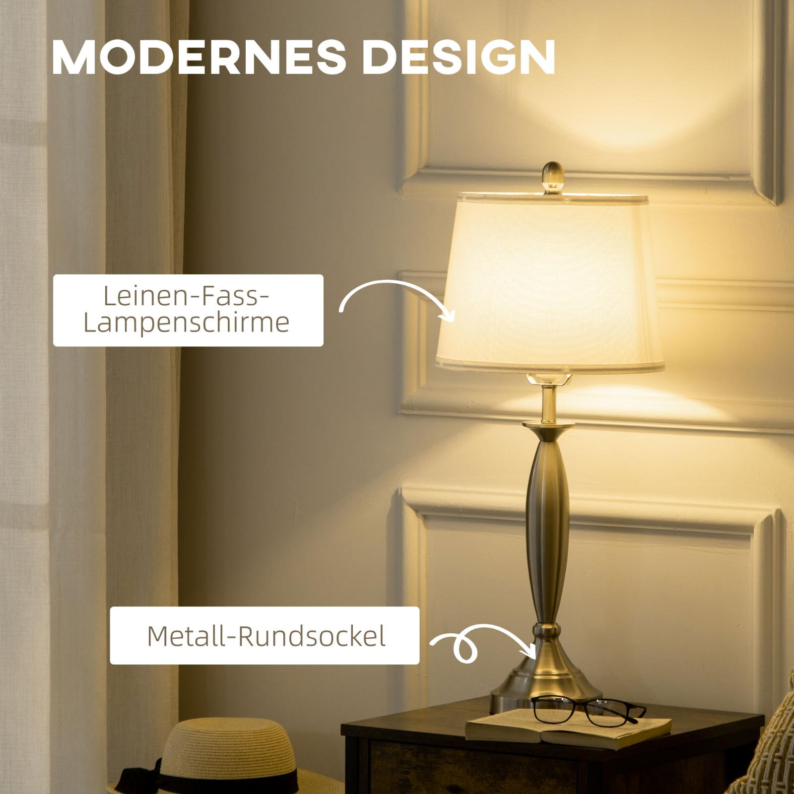 Eine Tischlampe mit weißem Lampenschirm und Metallsockel, neben Hut, Buch und Brille auf einem Tisch.