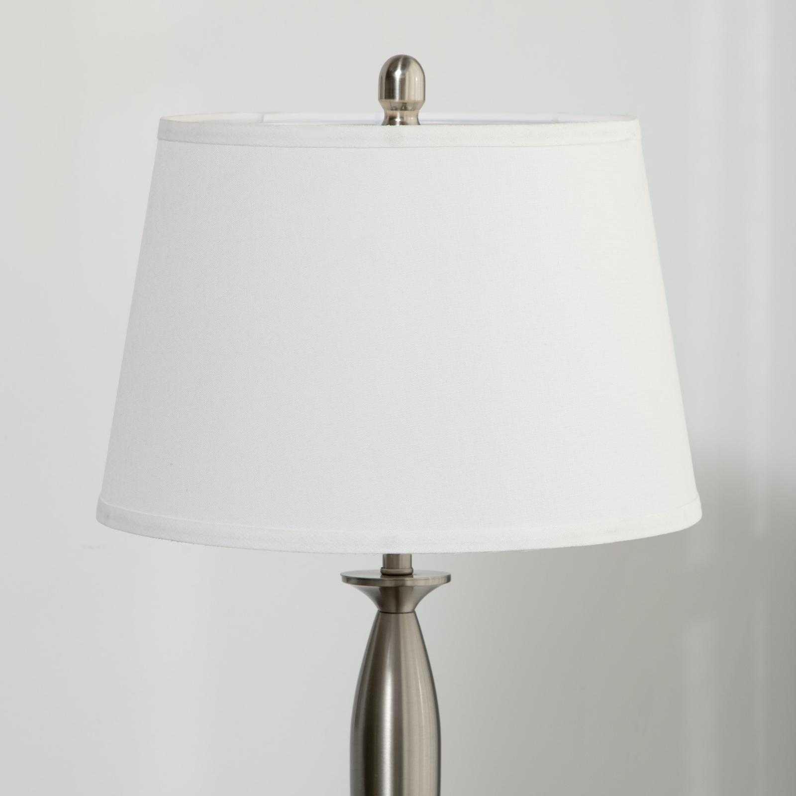 Nahaufnahme einer Tischlampe mit weißem Lampenschirm und silbernem Sockel. Der Hintergrund ist weiß.