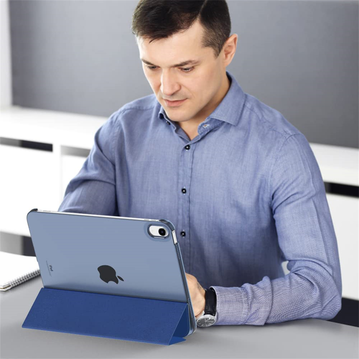 Ein Mann benutzt ein iPad in einer blauen Hülle. Das iPad liegt auf einem Schreibtisch. Der Mann konzentriert sich auf den Bildschirm.