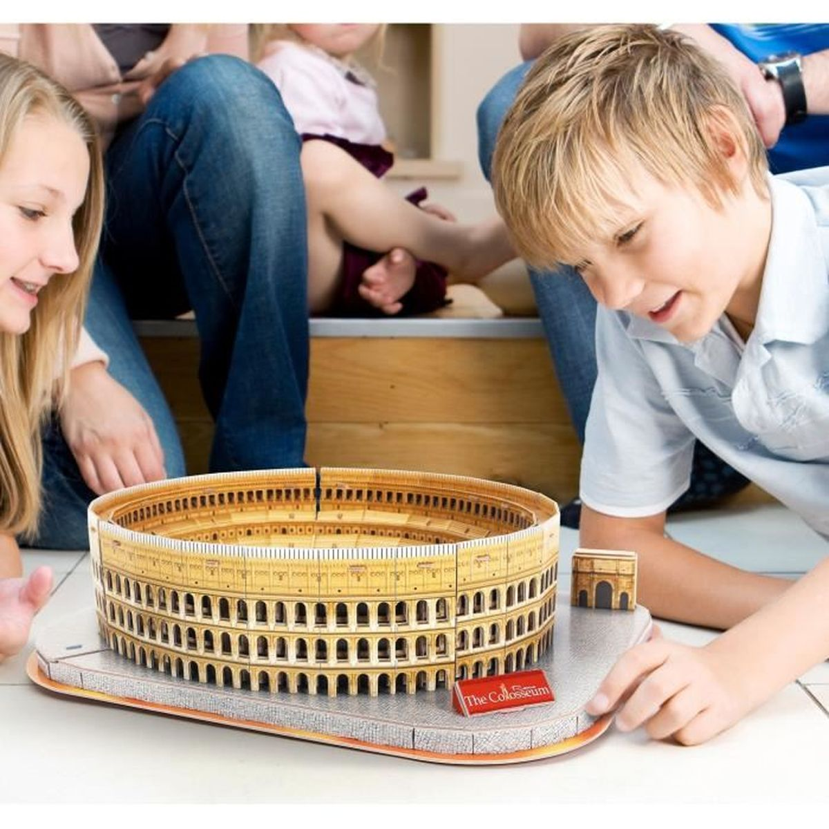 Una famiglia interagisce con un modello del Colosseo. Il modello è su una superficie grigia, sfondo sfocato.