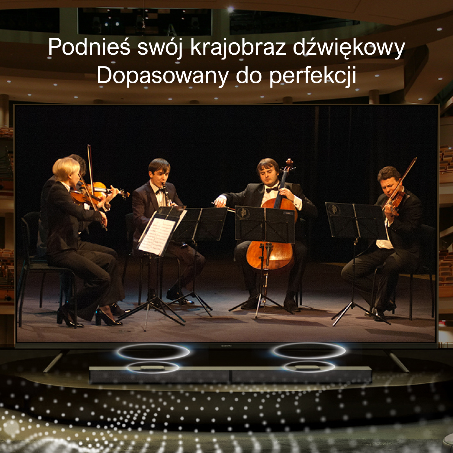 Orkiestra gra przed dużym ekranem. Ekran wyświetla rozmyty obraz sali koncertowej.