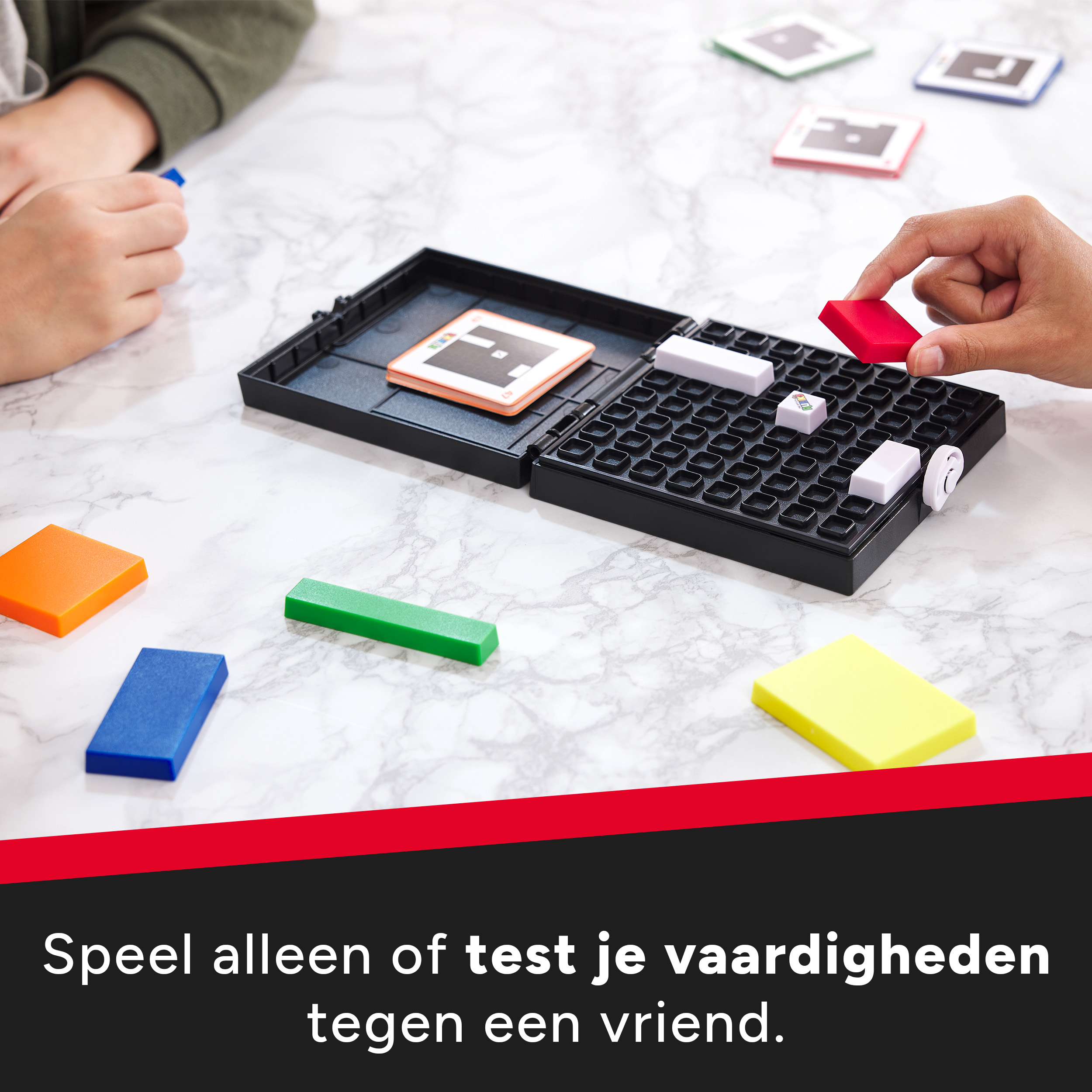 Dwie osoby grają w grę planszową. Kolorowe elementy. Gra jest w czarnej obudowie. Białe i kolorowe klocki.