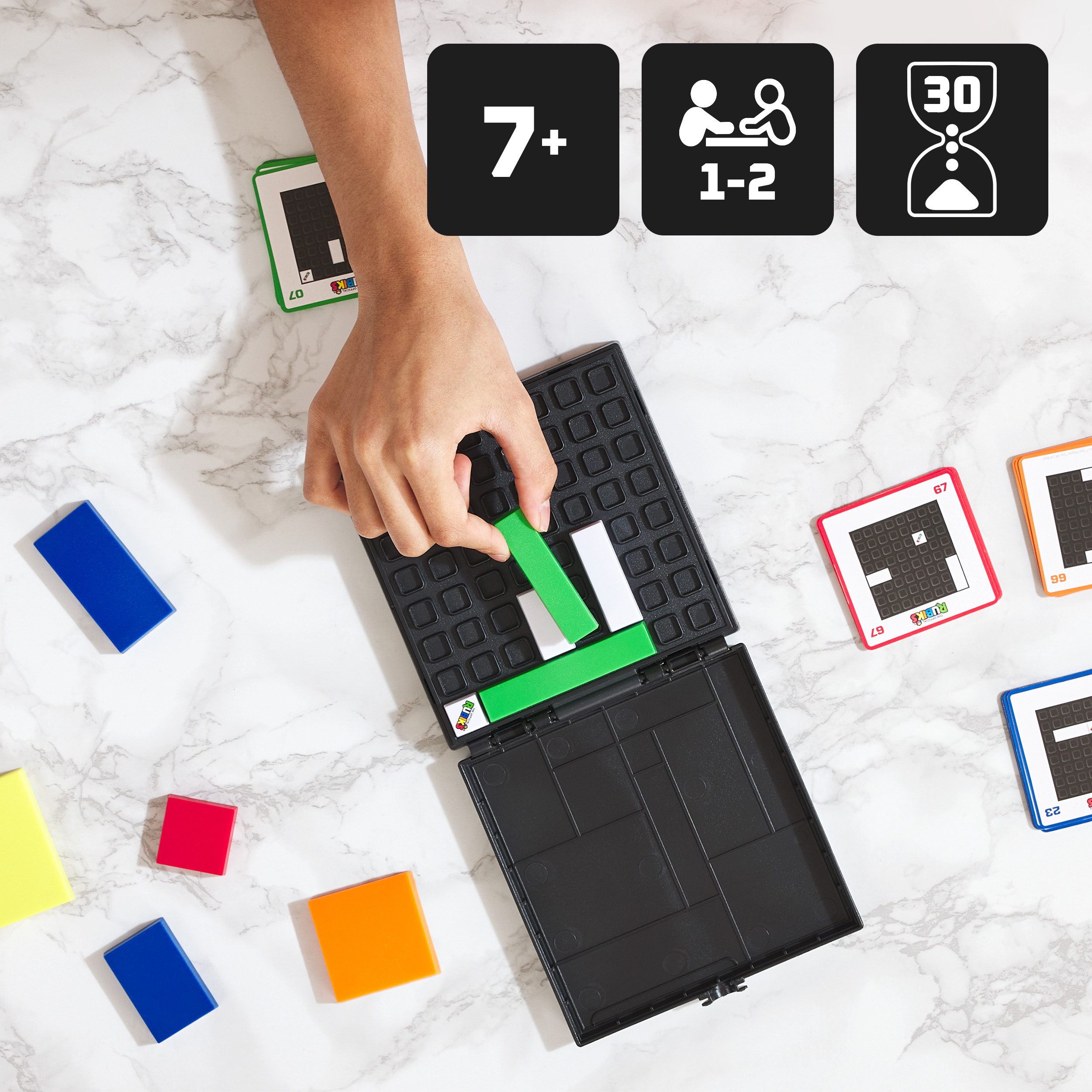 Osoba grająca w grę Rubik's Grid Lock. Kolorowe klocki i karty na białej marmurowej powierzchni.