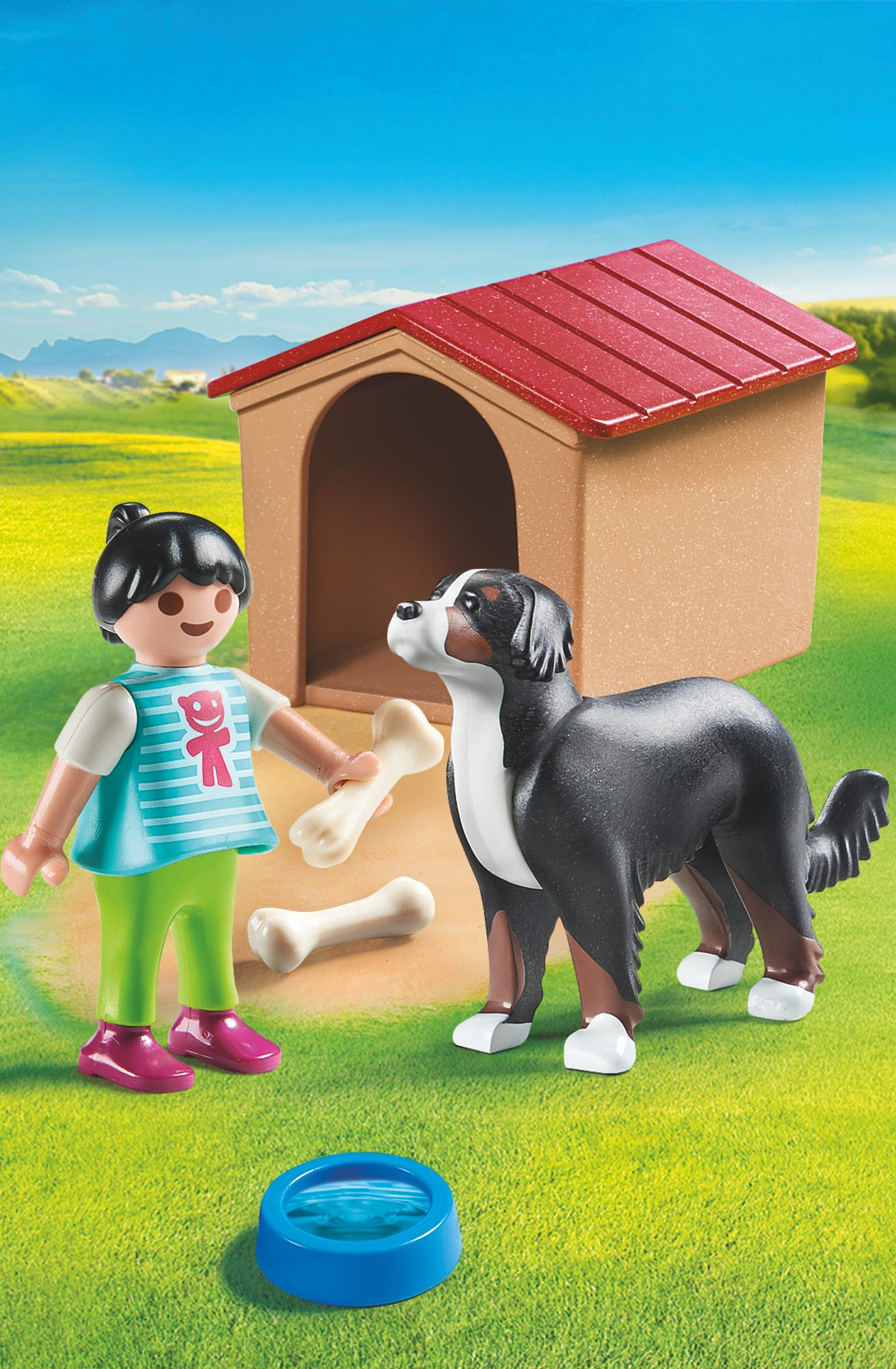 Una figura di Playmobil con un cane e una cuccia in un campo erboso sotto un cielo blu.